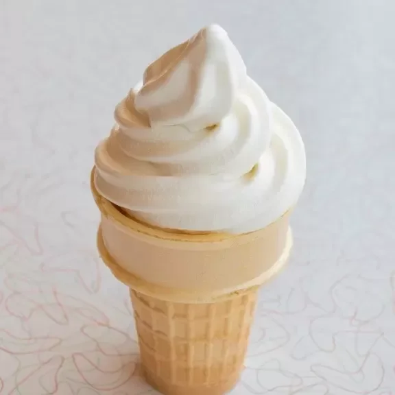 A soft serve vanilla ice cream cone on a light background.