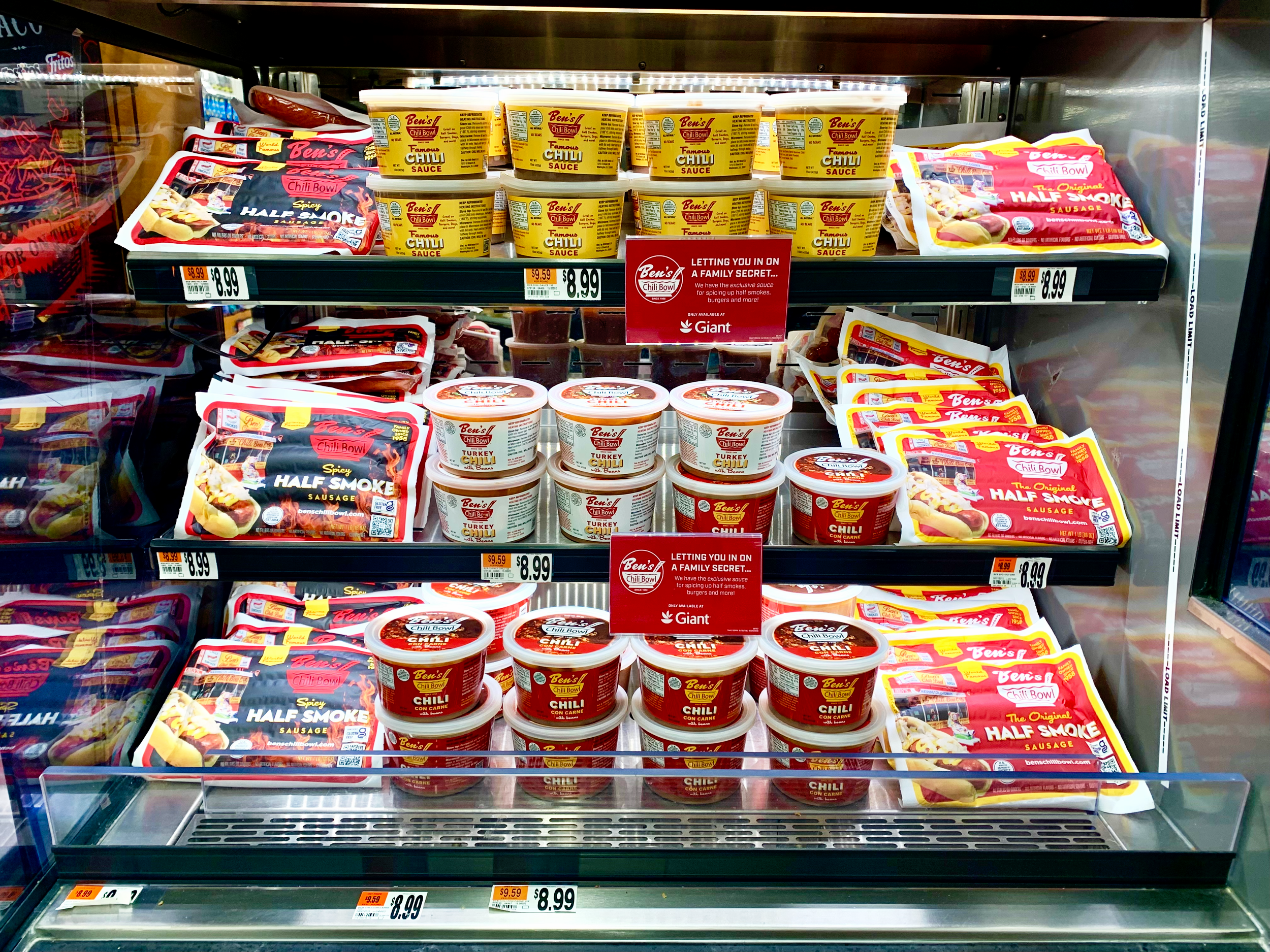 Assorted packages of Ben's Chili Bowl products, including half smoke sausages and chili, on refrigerated shelves in a grocery store.