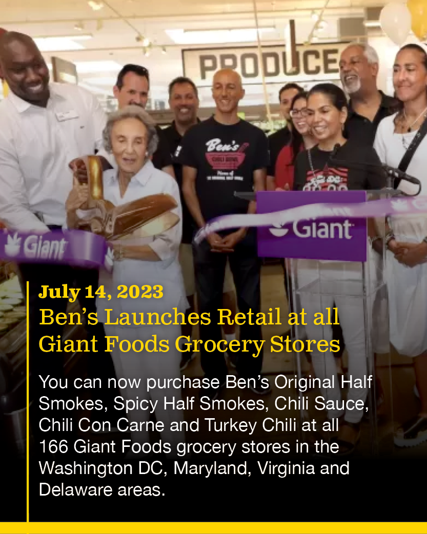 Group of people at a store opening event for Ben's retail launch at Giant Foods grocery stores, including an elderly woman holding a hot dog, with a sign behind them that reads "PRODUCE."