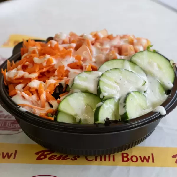 A bowl of salad with shredded carrots, chopped chicken, and sliced cucumbers with dressing.