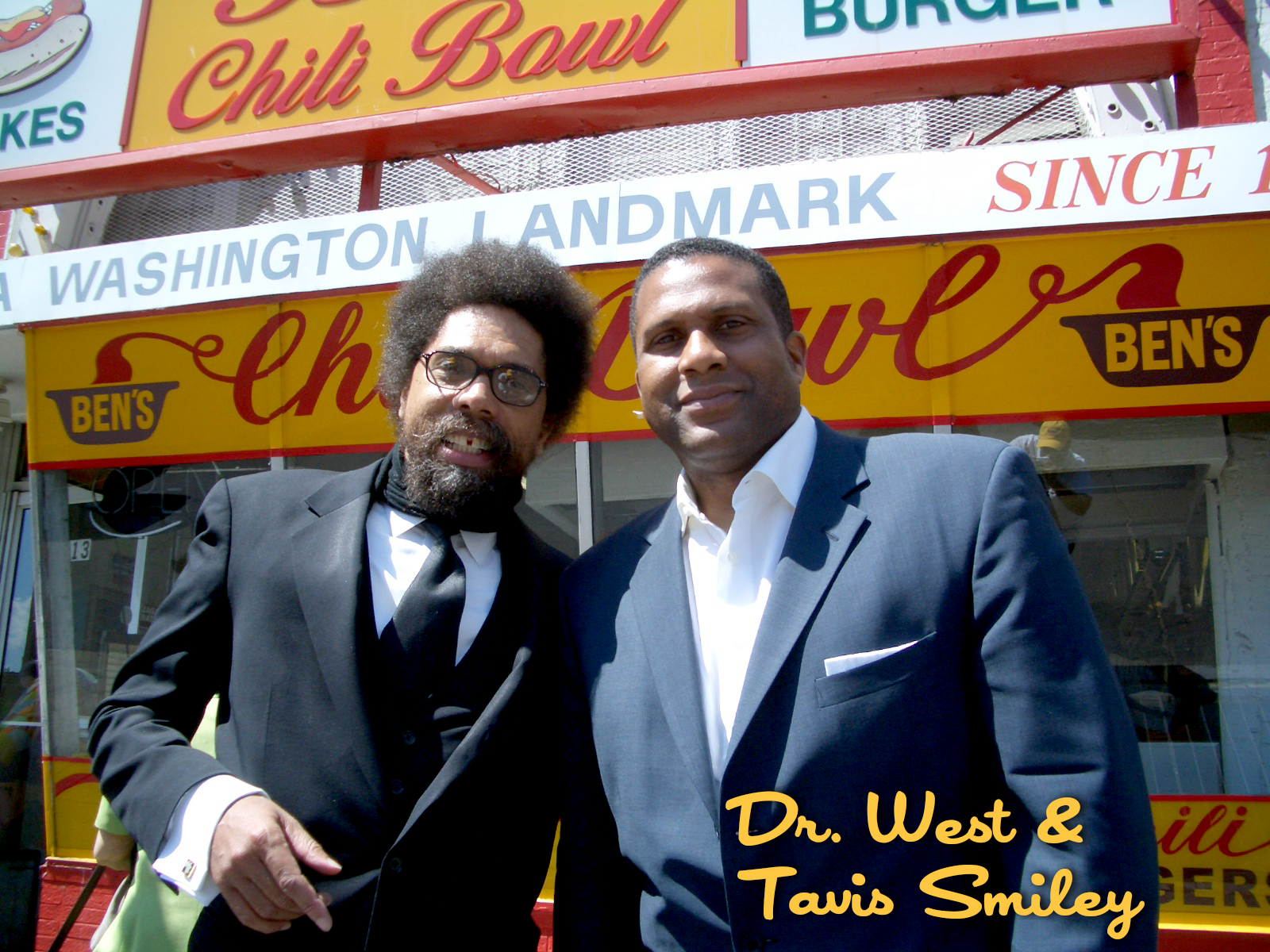 Two men dressed in suits standing outside a restaurant called Ben's Chili Bowl. One has an afro hairstyle and glasses, the other is clean-shaven with short hair. The photo has a text overlay that reads "Dr. West & Tavis Smiley."