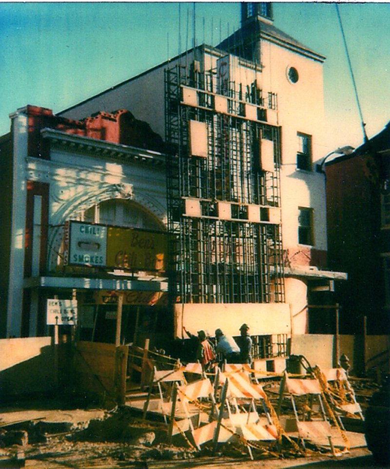 Street view of a building under construction with scaffolding and workers, with a sign for a business called 'Celt Smoke,' and construction barriers in the foreground.