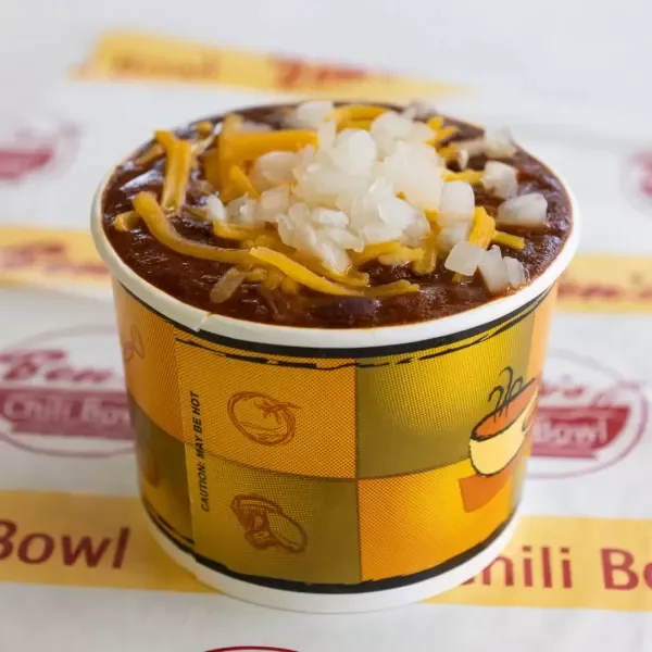 Cup of chili topped with shredded cheese and diced onions.