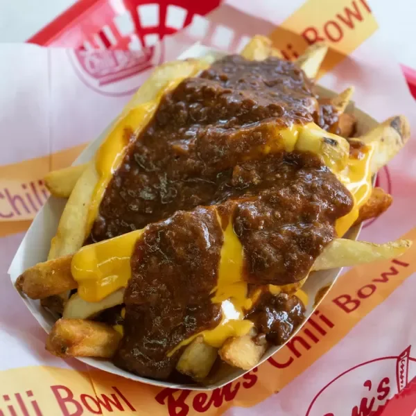 Chili cheese fries in a paper tray at Ben's Chili Bowl, topped with chili and melted cheese.