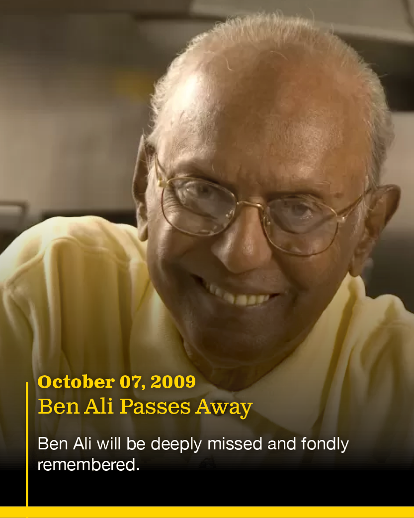 A portrait of an elderly man with glasses, smiling and wearing a yellow shirt. The image has text overlay mentioning the date October 07, 2009, and the note 'Ben Ali Passes Away,' indicating it's a tribute to Ben Ali, who is remembered fondly.