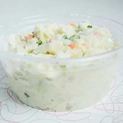 A bowl of potato salad with chopped vegetables on top, placed on a patterned surface.