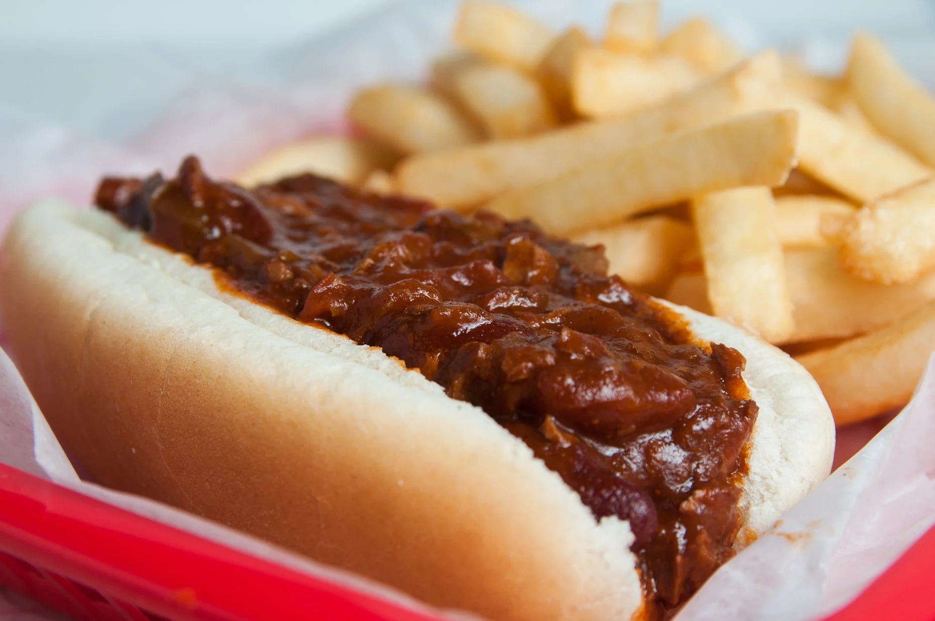 A hot beef chili dog in a soft bun served with a side of French fries.