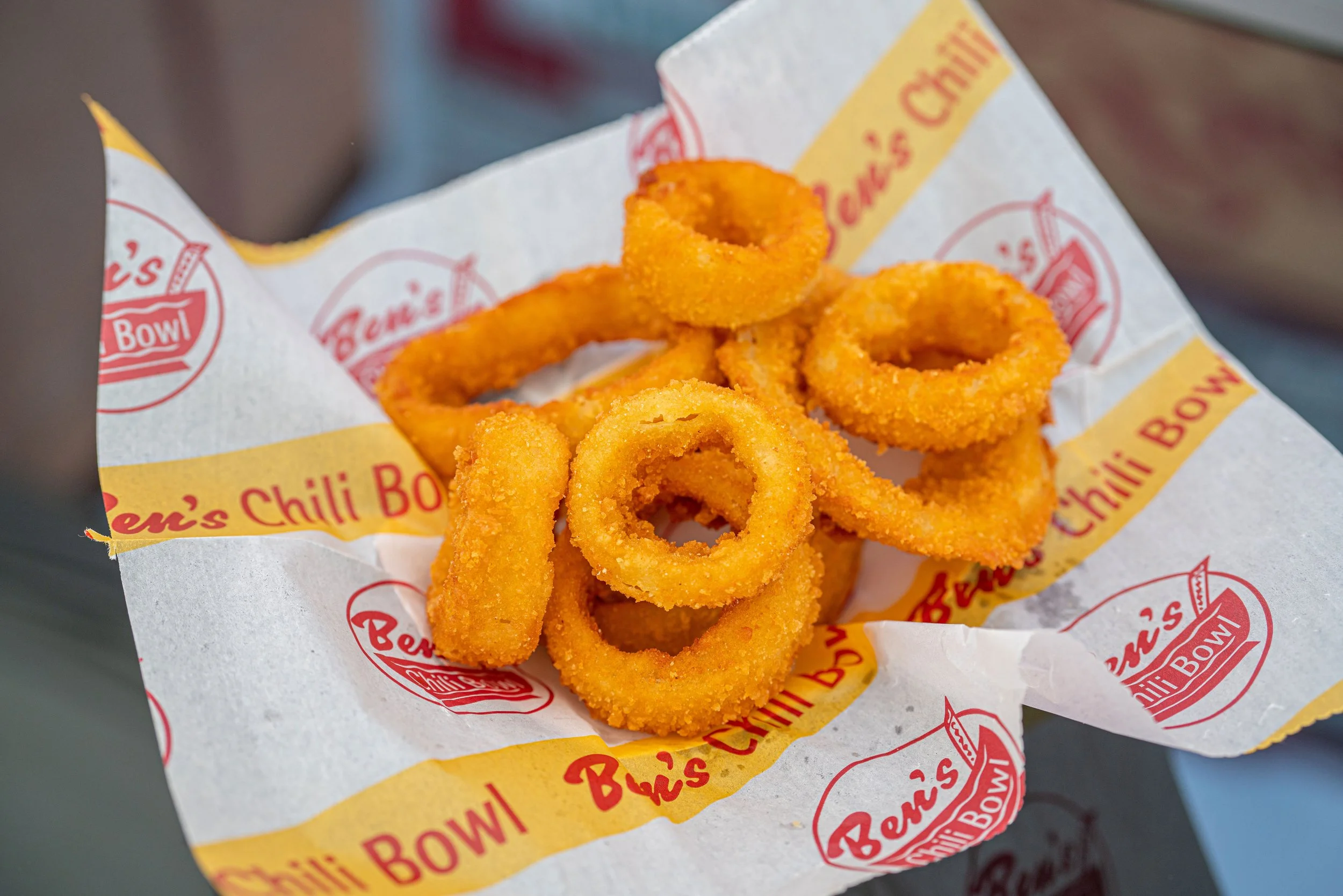 A serving of golden fried onion rings on Ben's Chili Bowl branded paper.