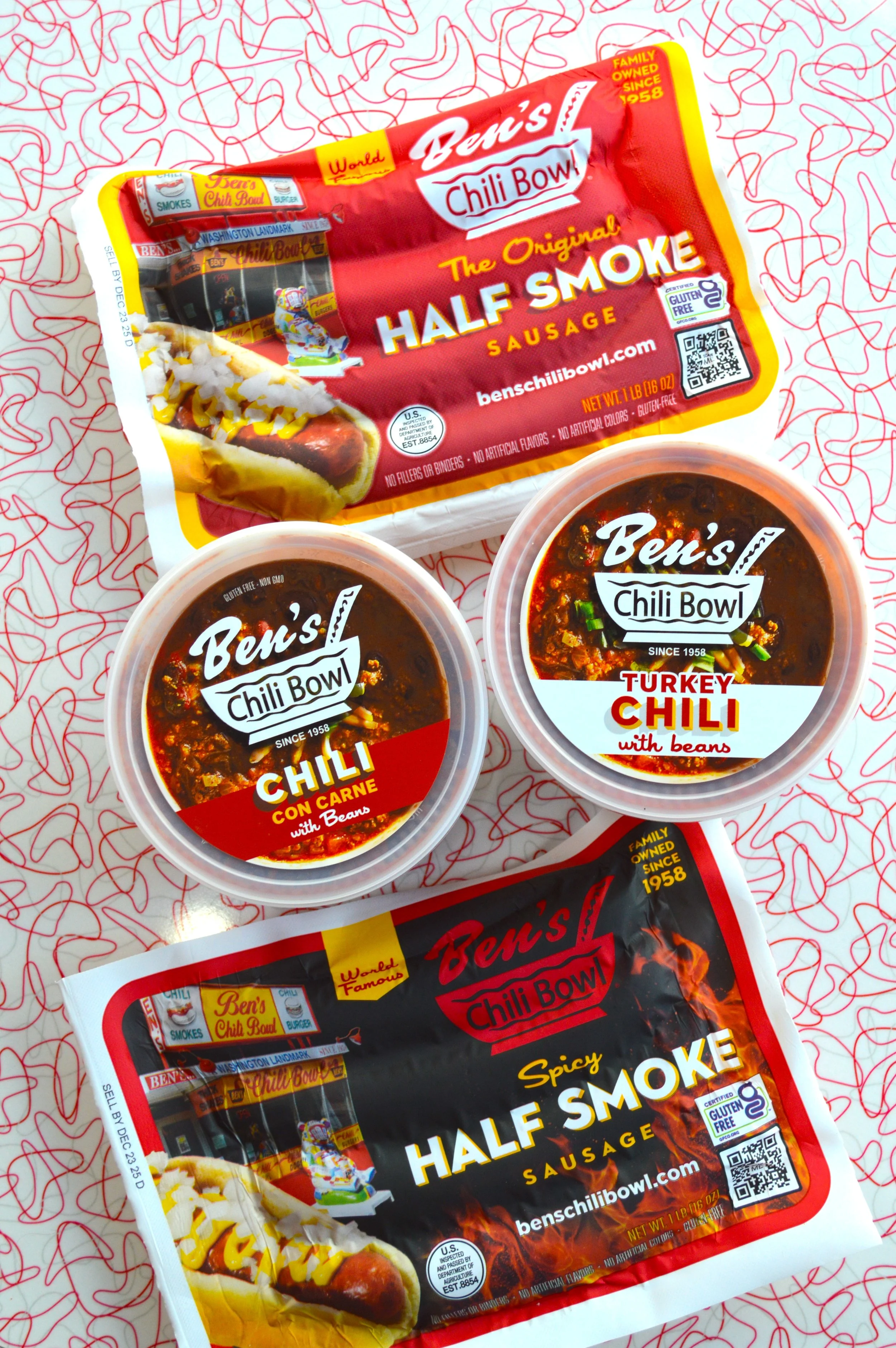 Various Ben's Chili Bowl packaged foods, including chili con carne and turkey chili with beans, on white paper with red squiggly lines pattern.