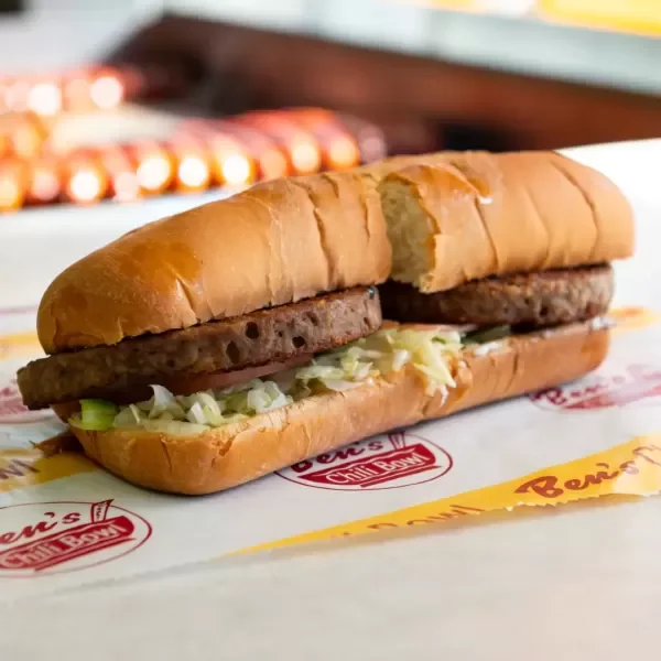 A cheeseburger sub with lettuce and hamburger patty in a bun, resting on branded paper.