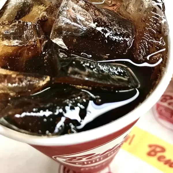 A cup filled with ice cubes and dark soda, likely cola.