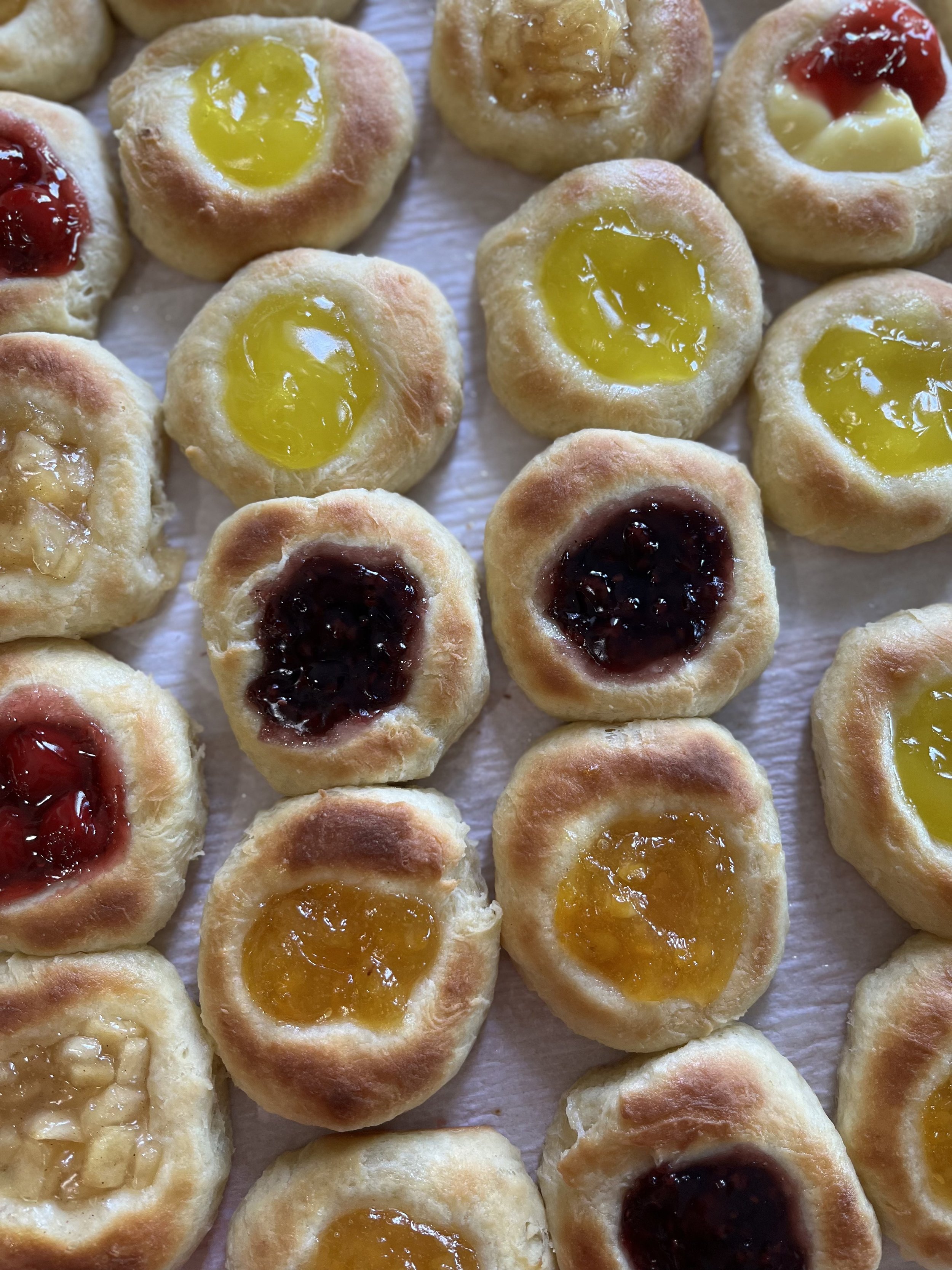 Rows of kolacheswith toppings of fruit preserves or jams, including lemon, cherry, and raspberry fillings.