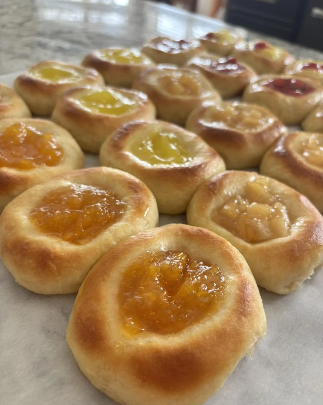 Assorted baked kolaches with fruit jam toppings, including apricot, lemon, and raspberry flavors, on a baking sheet from Sixth Street Kolaches in Nebraska.