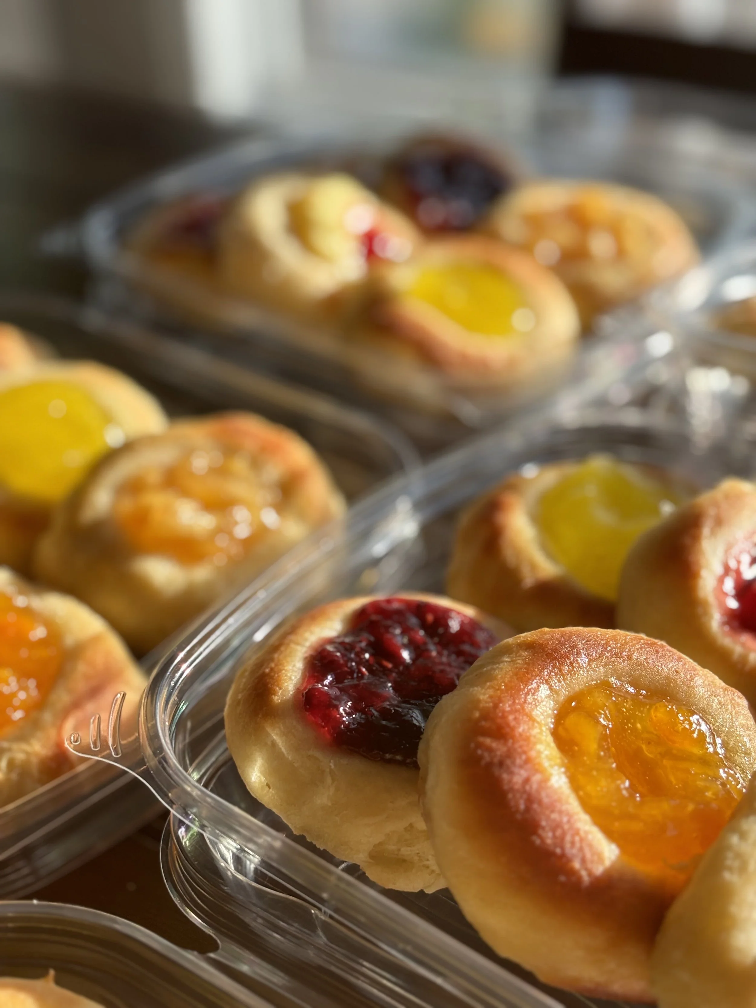 Close-up of Czech kolaches with different fruit toppings in clear plastic containers.