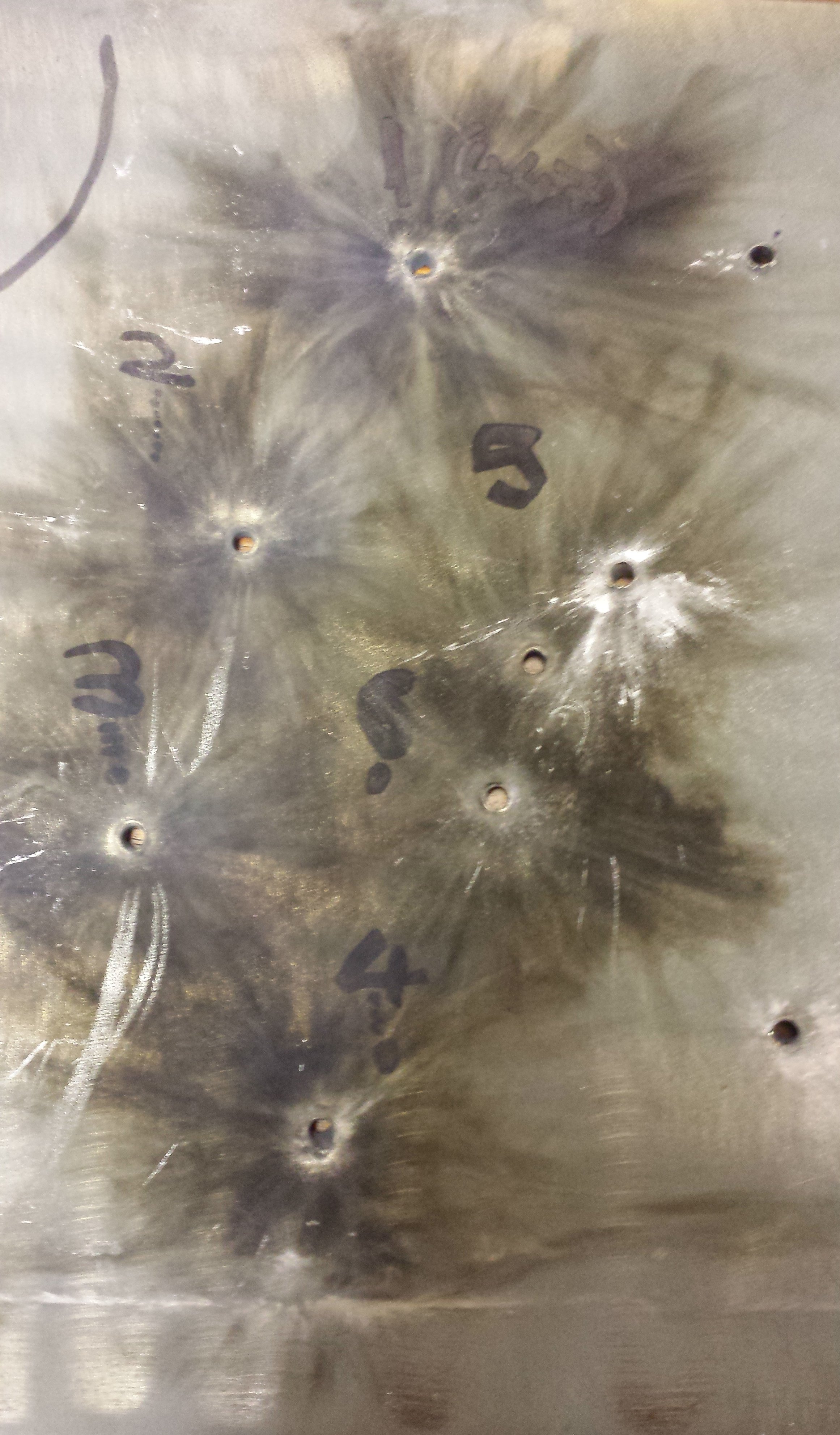 A metallic surface with multiple small holes and numbered markings from 1 to 5, with streaks and marks around the holes, possibly indicating welding or drilling points.