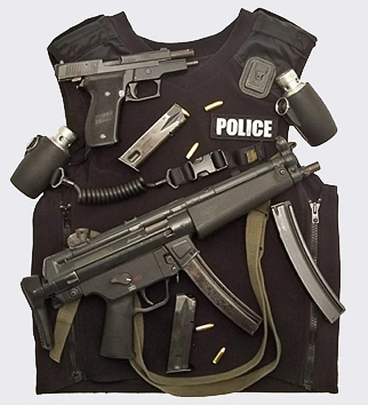 Police tactical vest with a handgun, ammunition, a radio, and a submachine gun attached.
