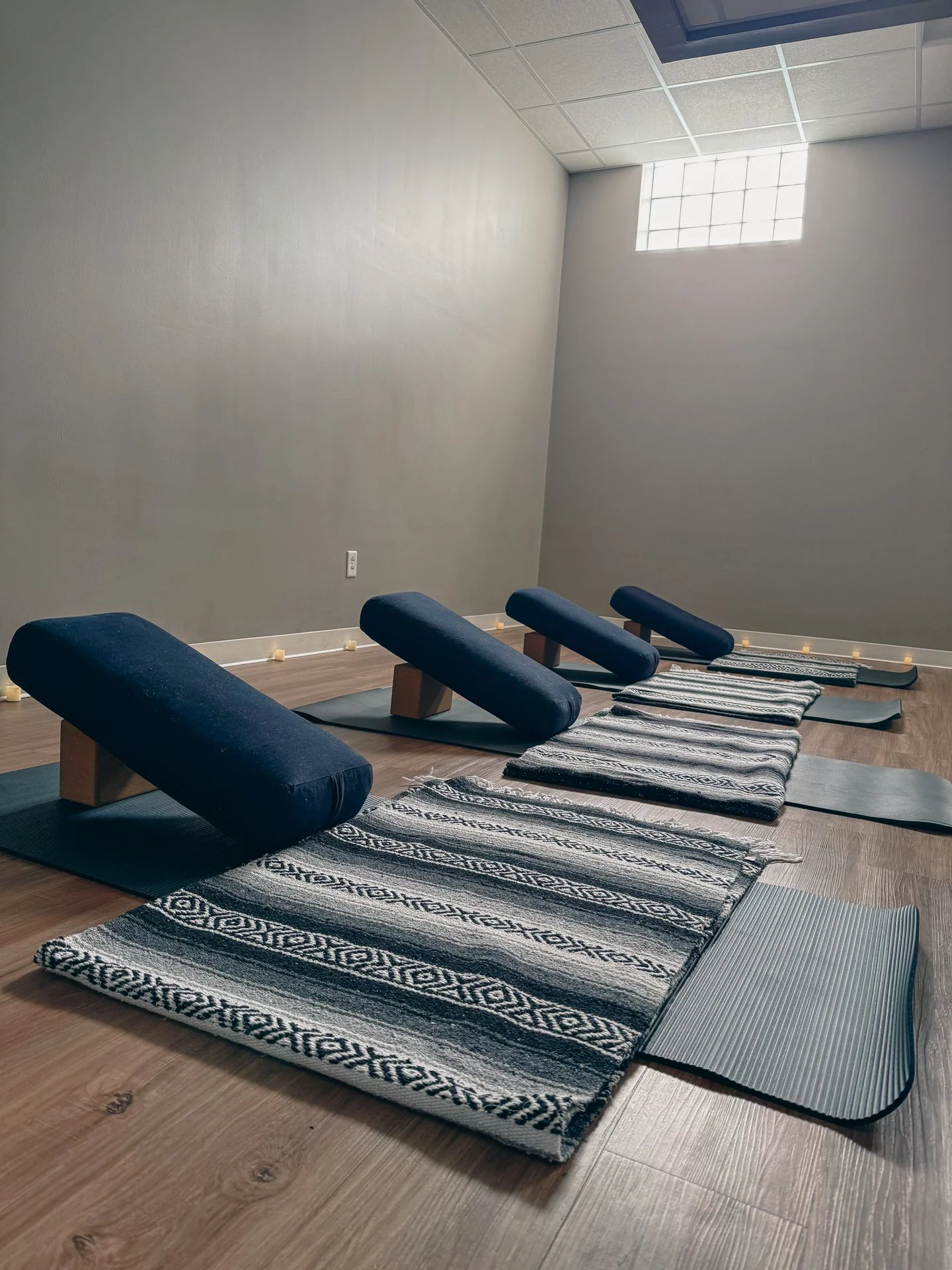 Photo of yoga studio room set up with yoga mats, bolsters, blocks, blankets, and candles for a restorative yoga class.