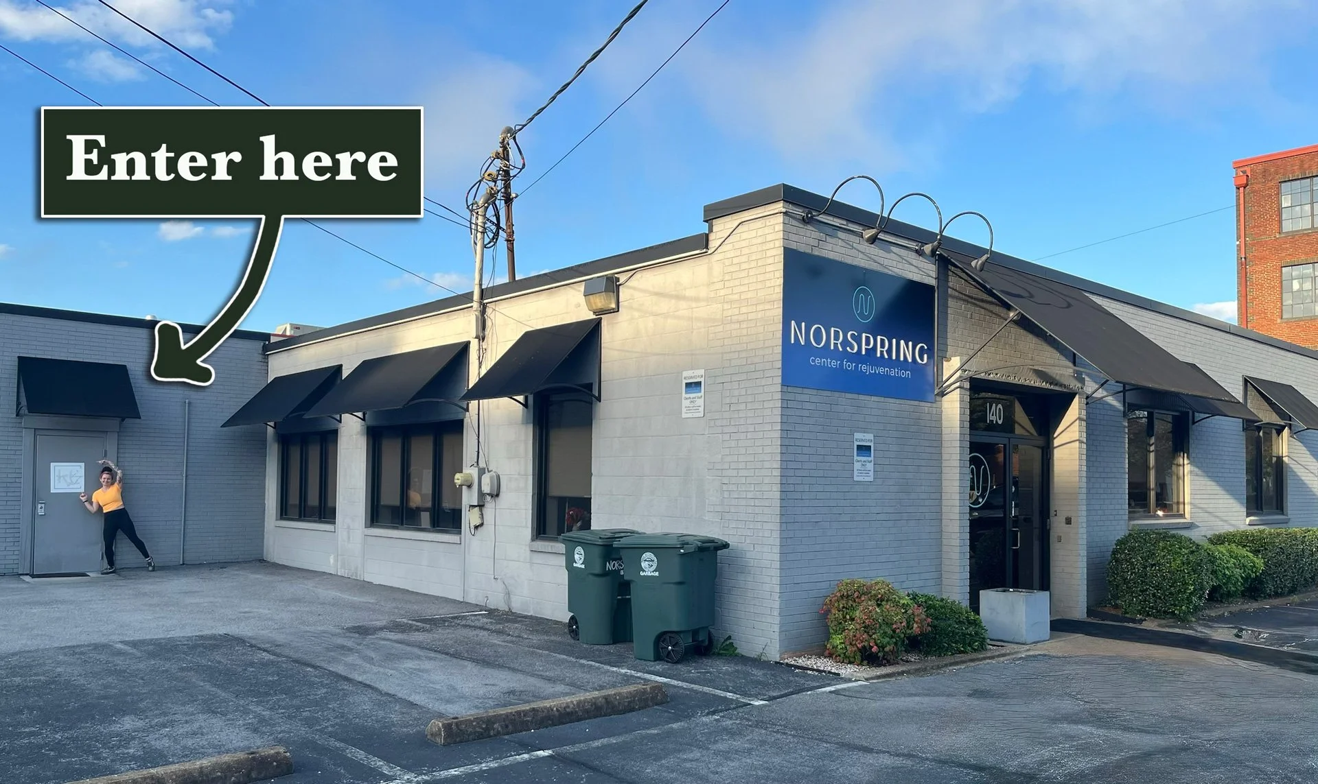 picture showing the north side of the Norspring Health & Wellness building, with Sara pointing to the side door to the left of the main entrance and "Enter here" text with an arrow overlaid onto the image.