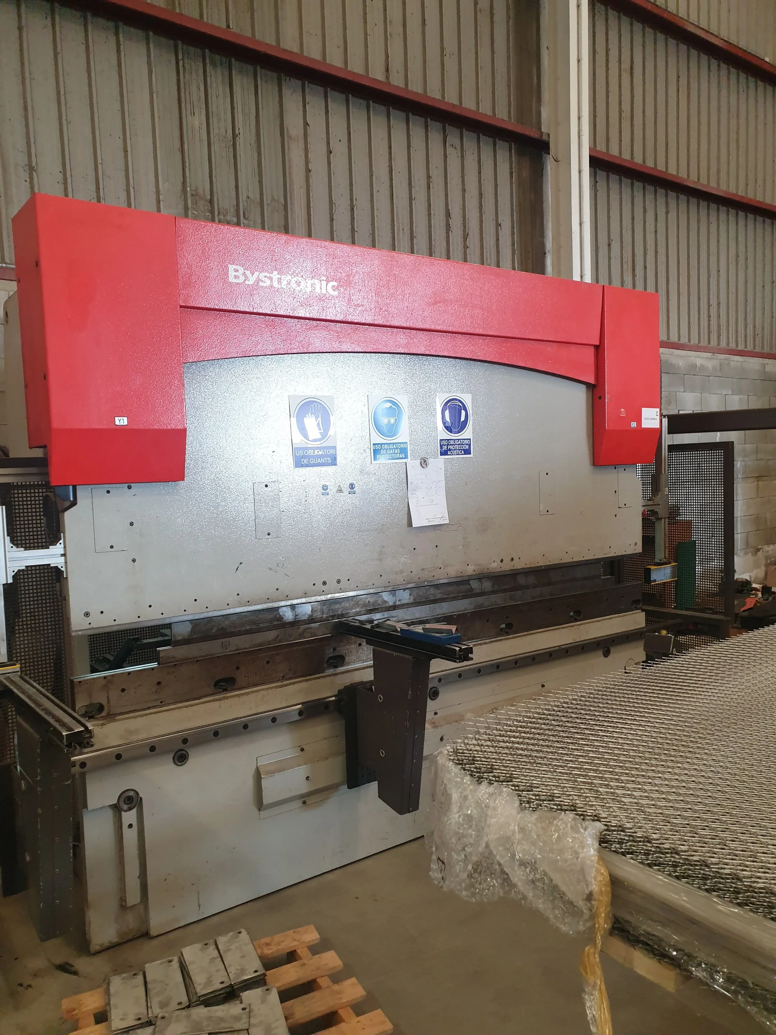 Máquina industrial de corte con instrucciones para uso de guantes, protección auditiva y protección de gafas de seguridad en un entorno de fábrica.