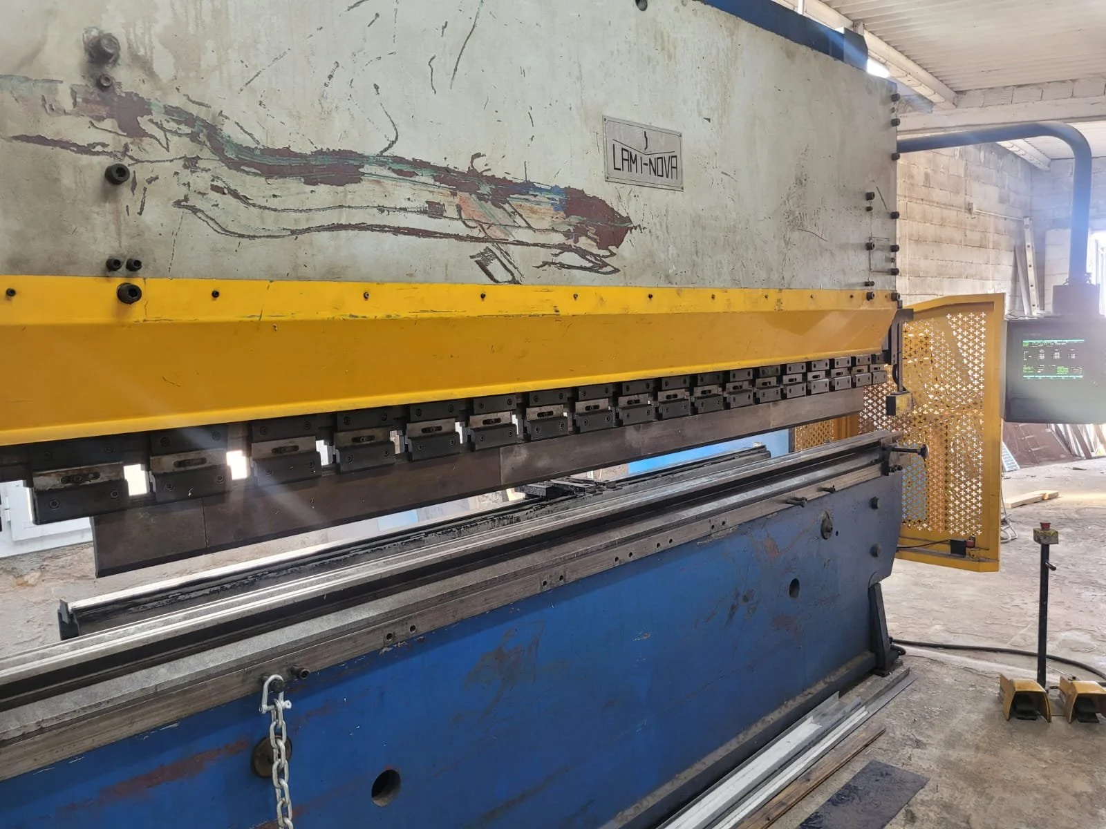 Una máquina de corte de metal industrial de color azul y amarillo en un taller, con un monitor digital y un espacio de trabajo.