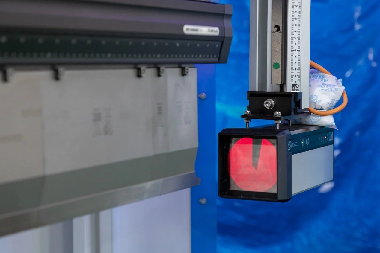 Dispositivo de medición láser con pantalla que muestra un haz rojo en un ambiente industrial.