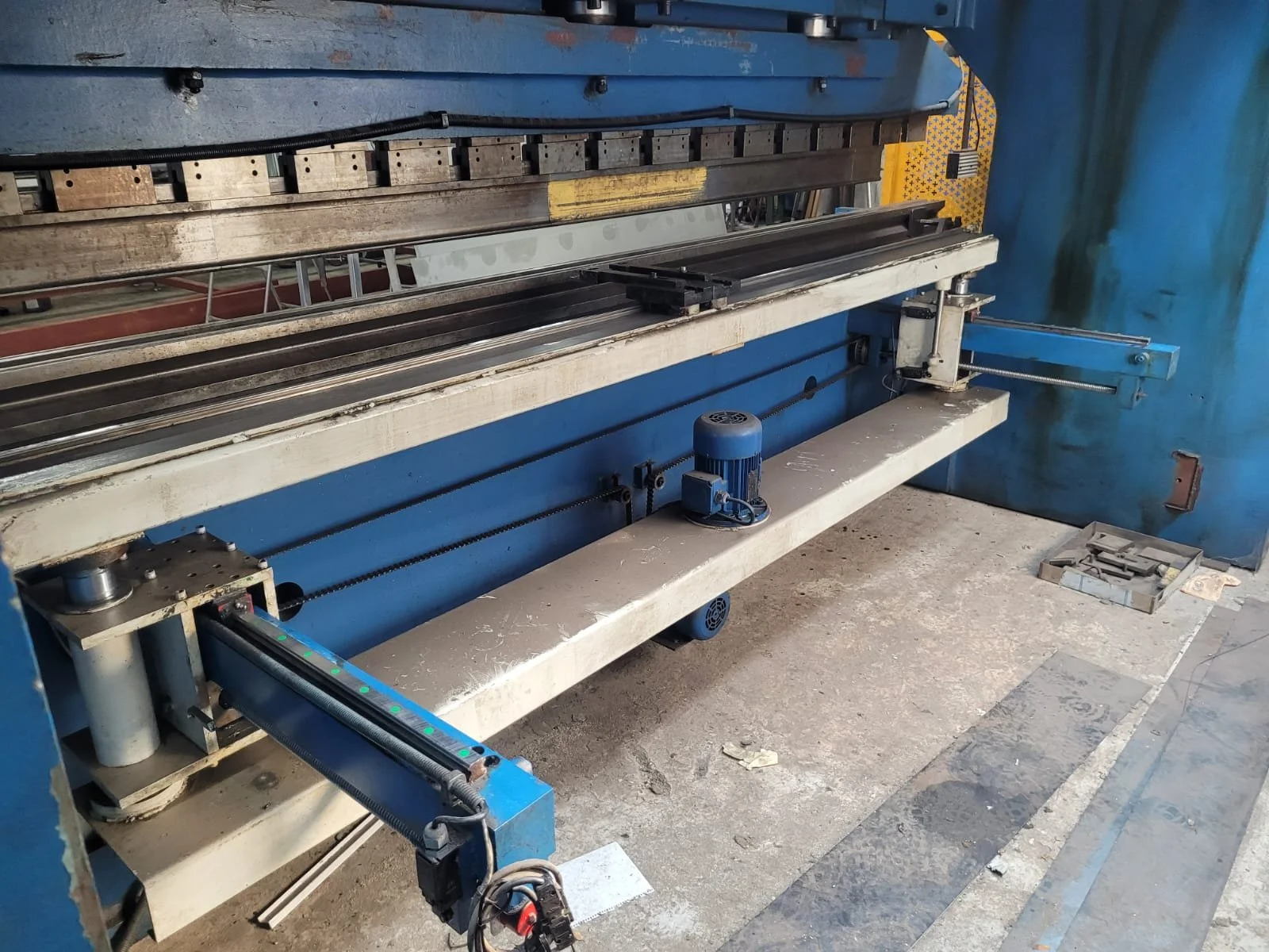 Máquina industrial de metal en un taller con piso de concreto y paredes azules.