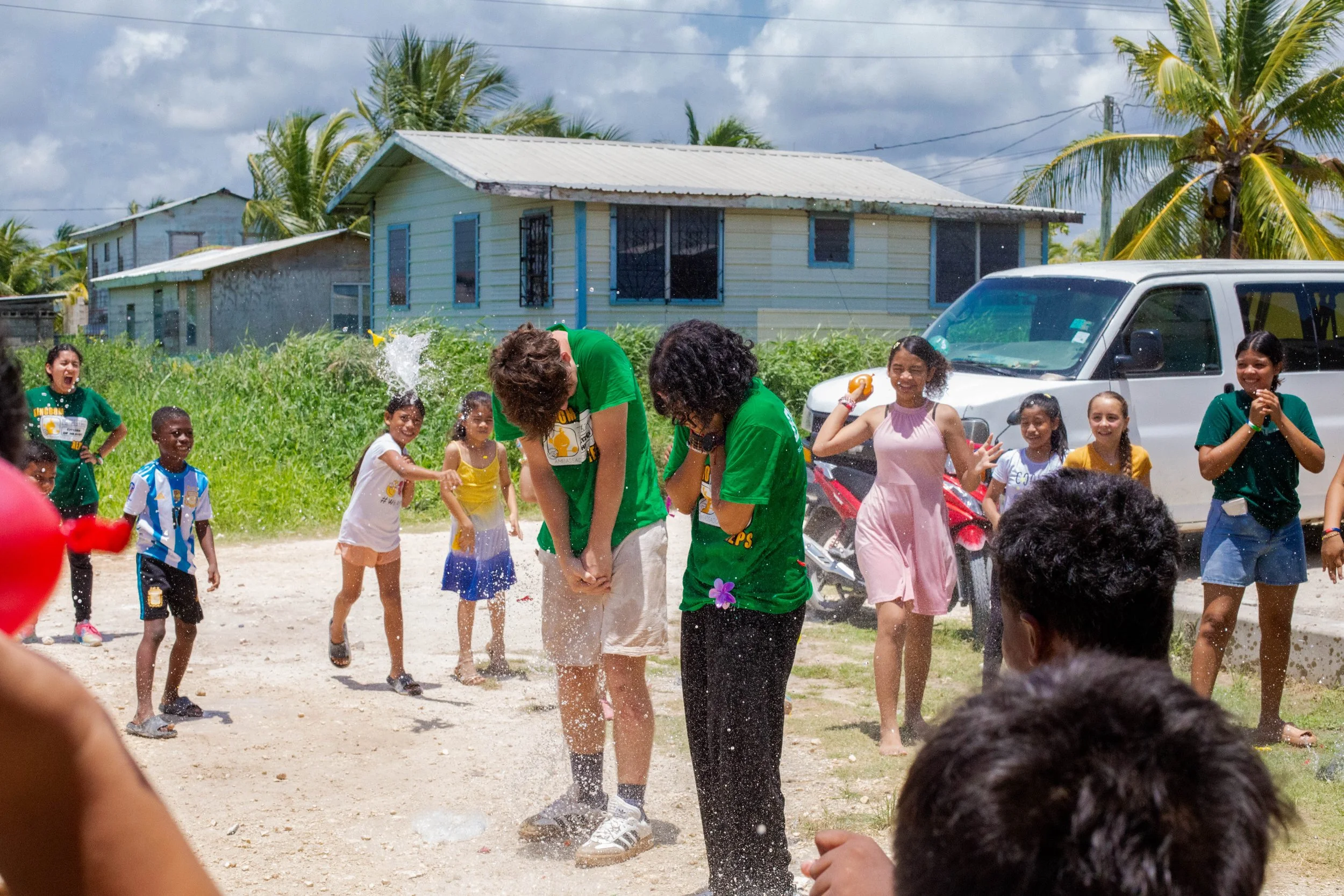 Children playing with hula hoops and engaging in outdoor activities on a school playground with a mint green building in the background.