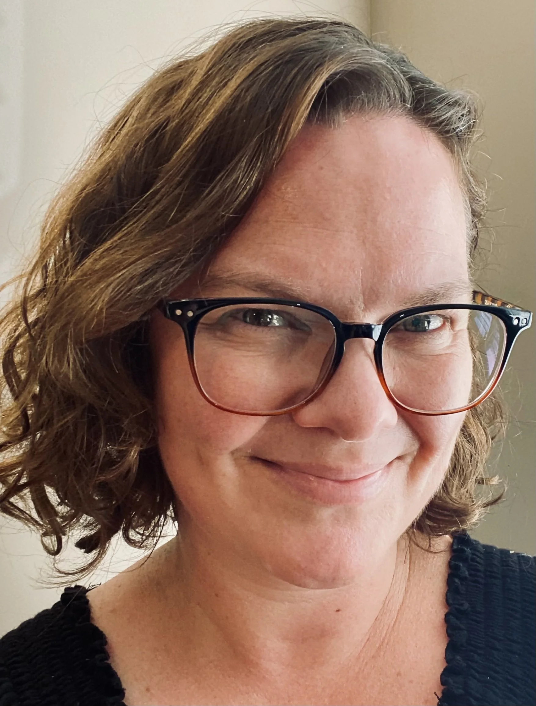 A woman with short, curly brown hair and glasses, smiling.