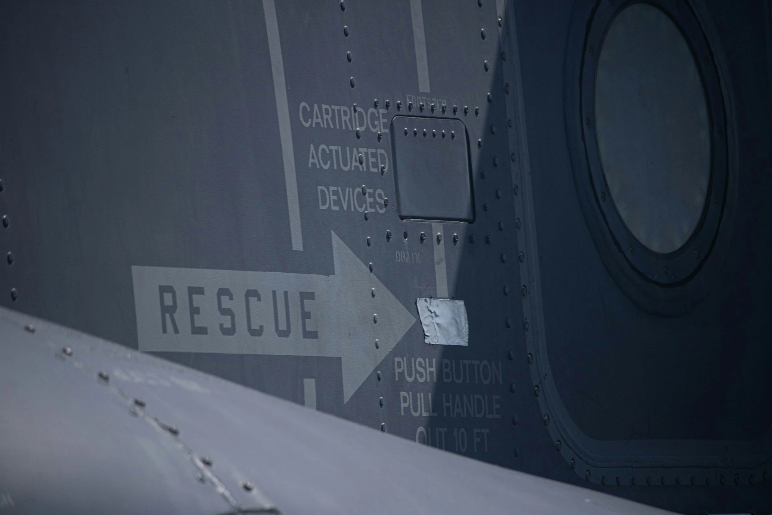 Inside view of a military aircraft with inspection and rescue instructions painted on the metal surface, including a large arrow pointing to the right with the word 'RESCUE' and instructions for pushing a button and pulling a handle.