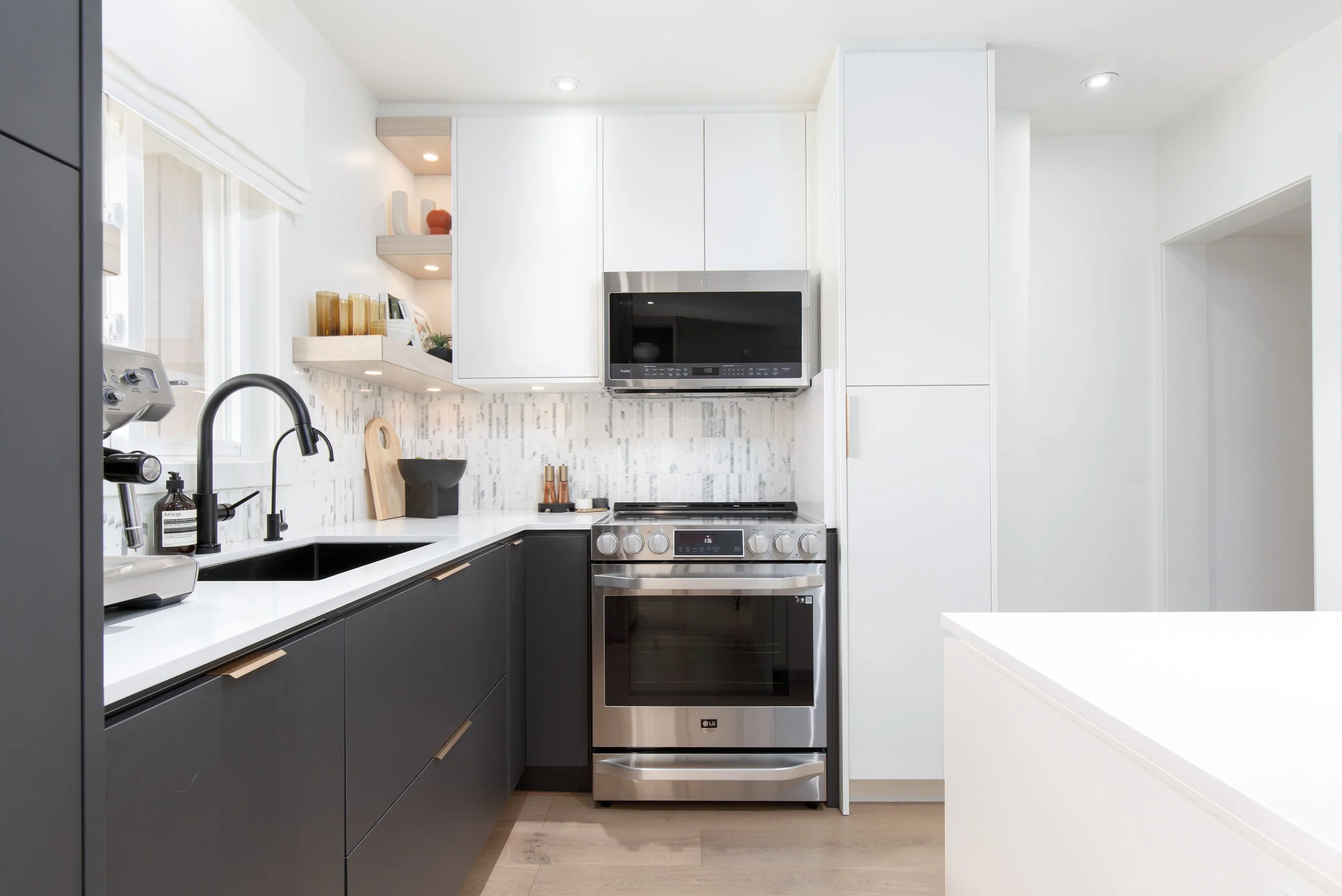Modern kitchen with black lower cabinets, white countertops, stainless steel oven and microwave, white upper cabinets, and a white tiled backsplash.
