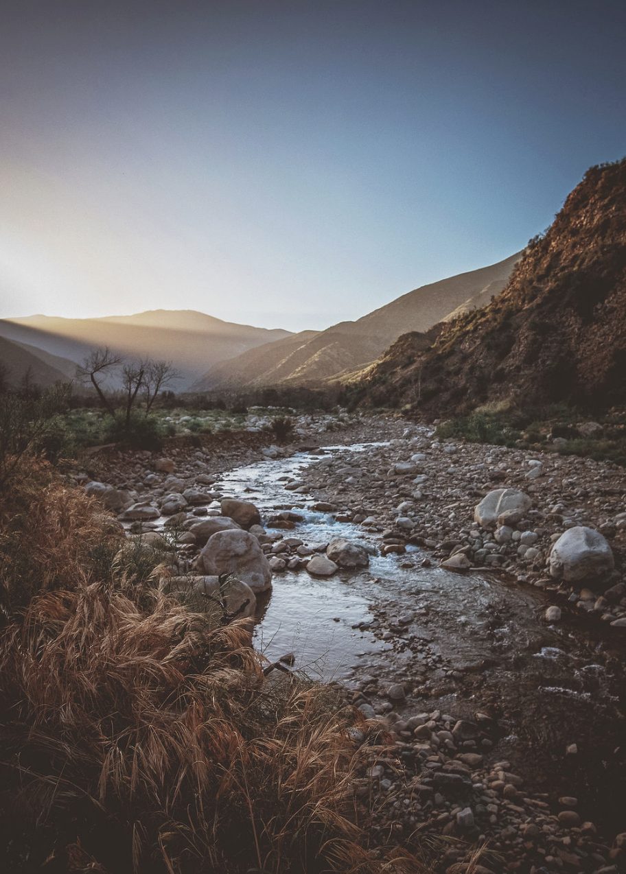 Scenic view of a rocky river flowing through a valley with mountains on either side, with a clear sky.