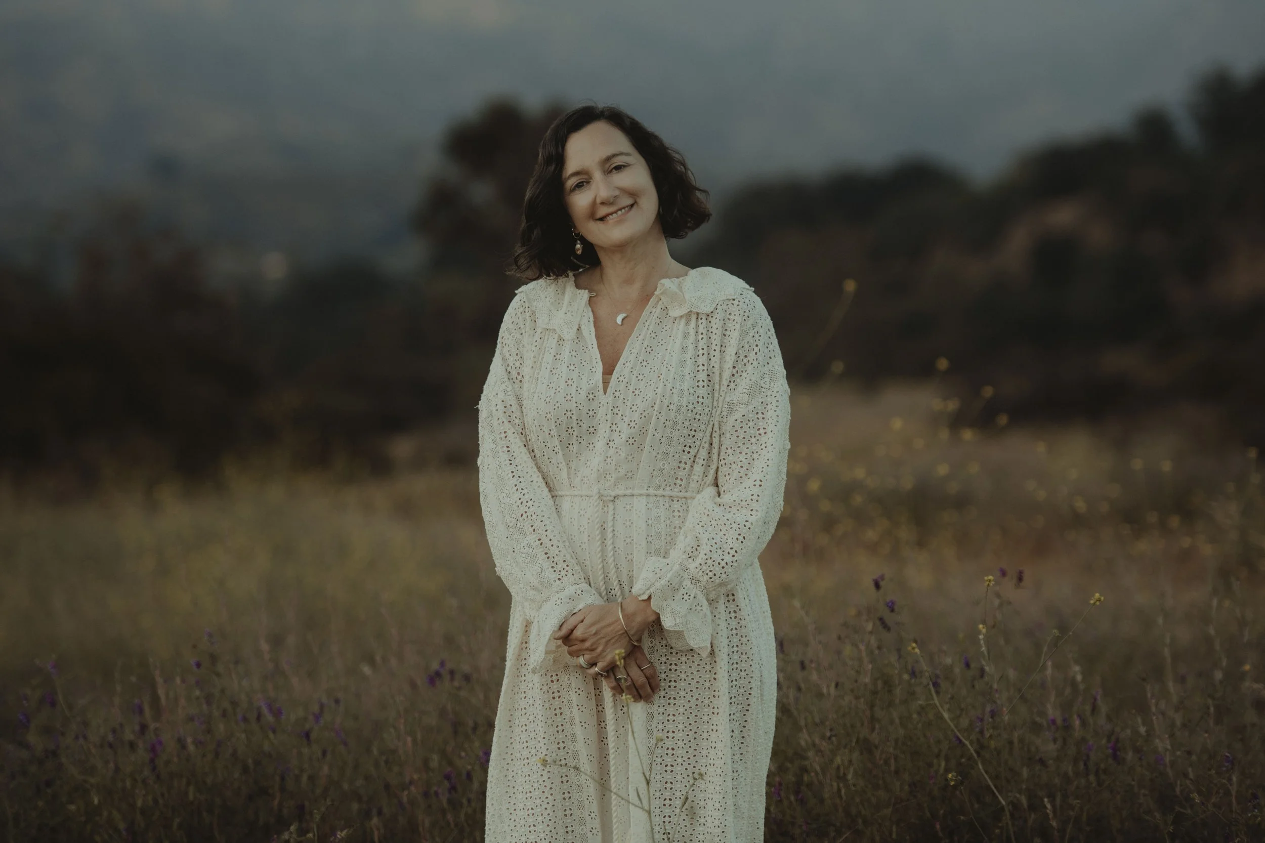 A portrait of Integrative Psychotherapist Yvonne Rendina standing in a grassy field with Ojai landscape in the background.
