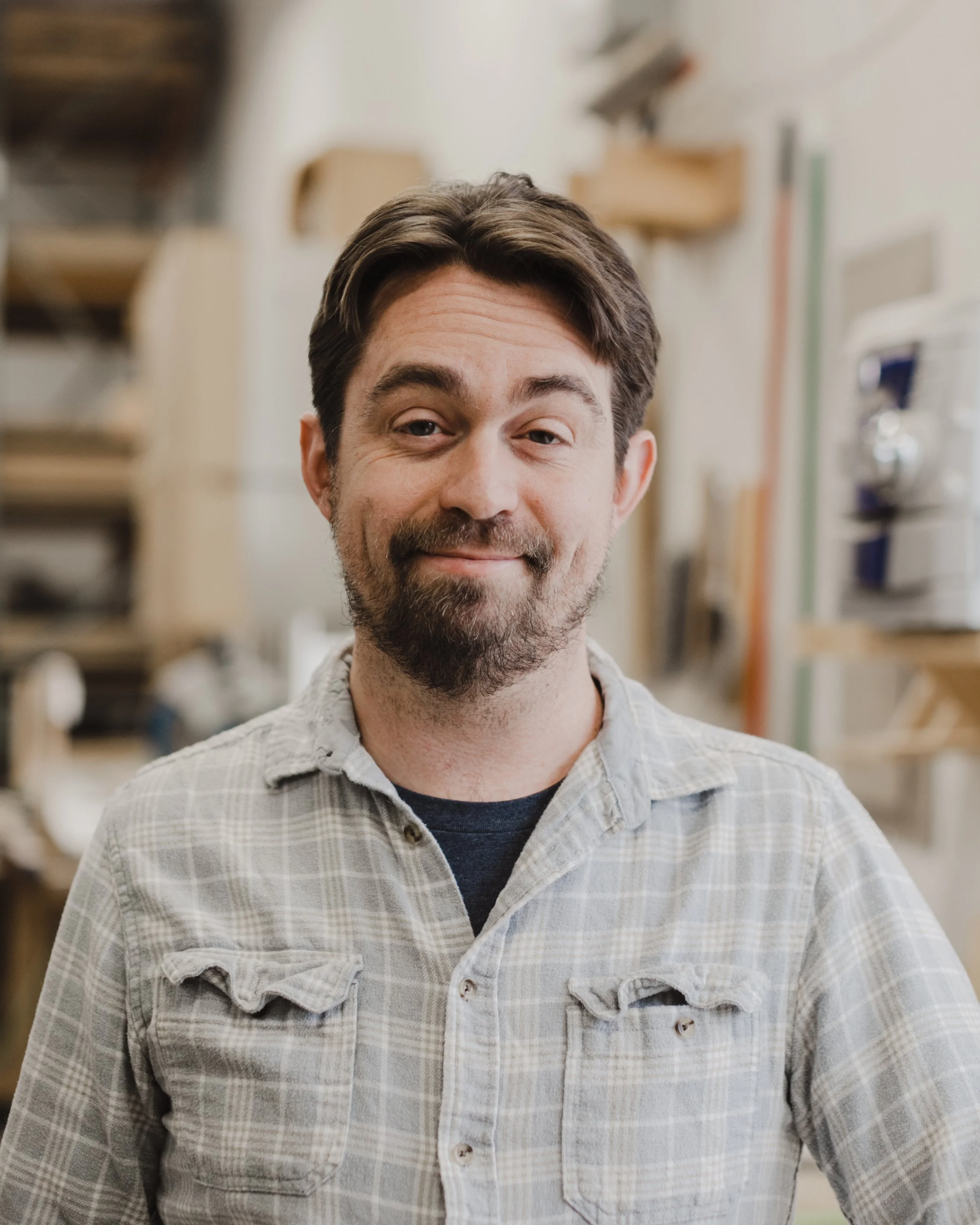A man with brown hair and a beard smiling in a workshop.
