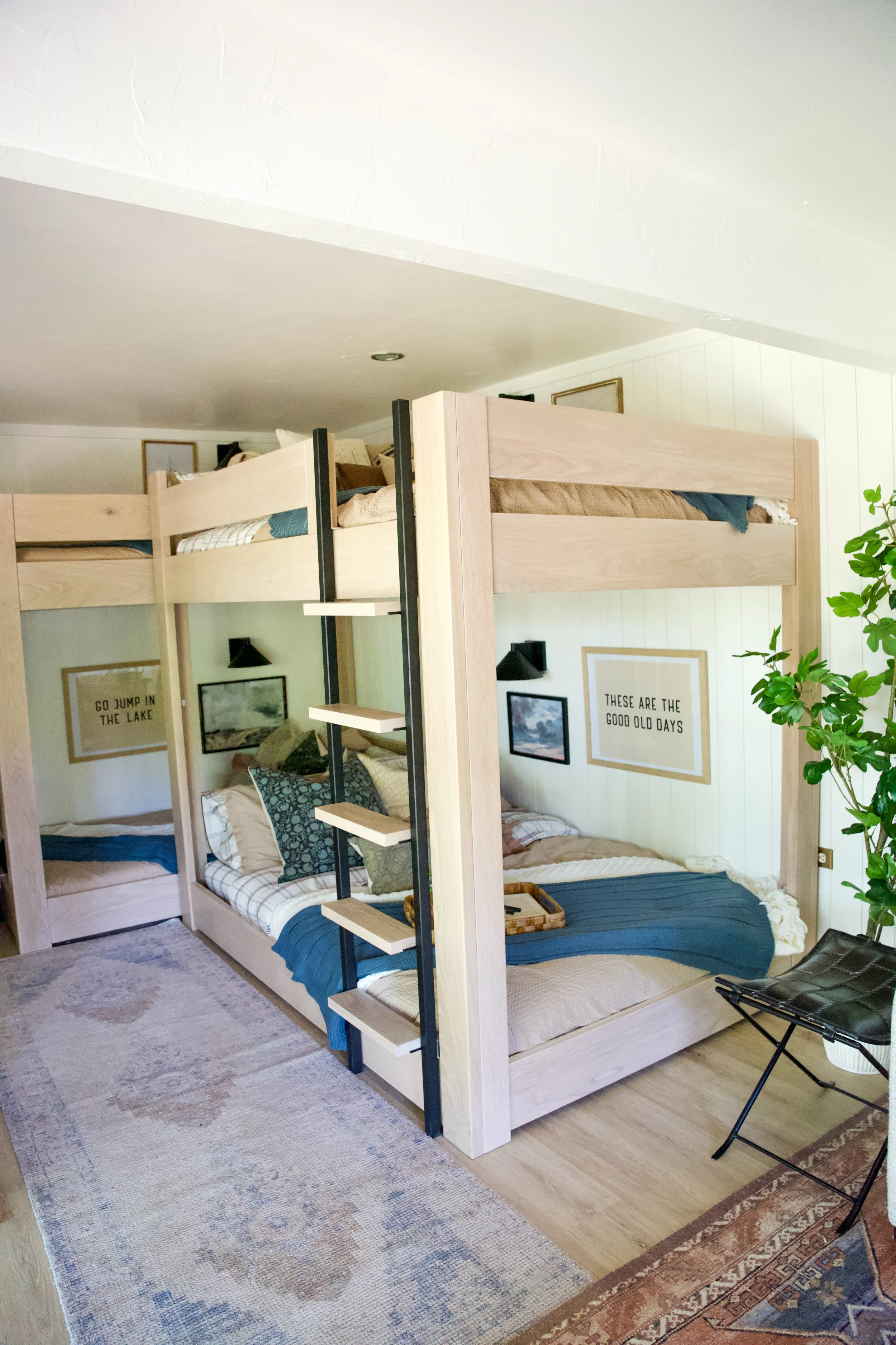 A bedroom with a wooden bunk bed that has a ladder, decorated with framed pictures and quotes on the wall, and a small plant in the corner.