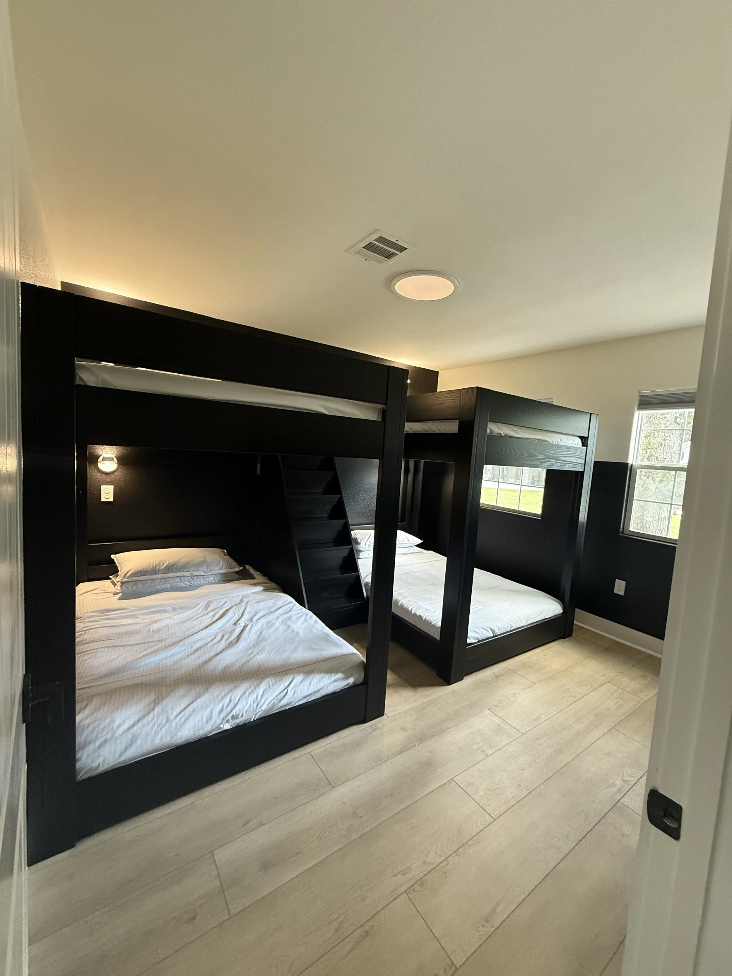 Bedroom with two black bunk beds with white bedding, wood floors, and windows letting in natural light.