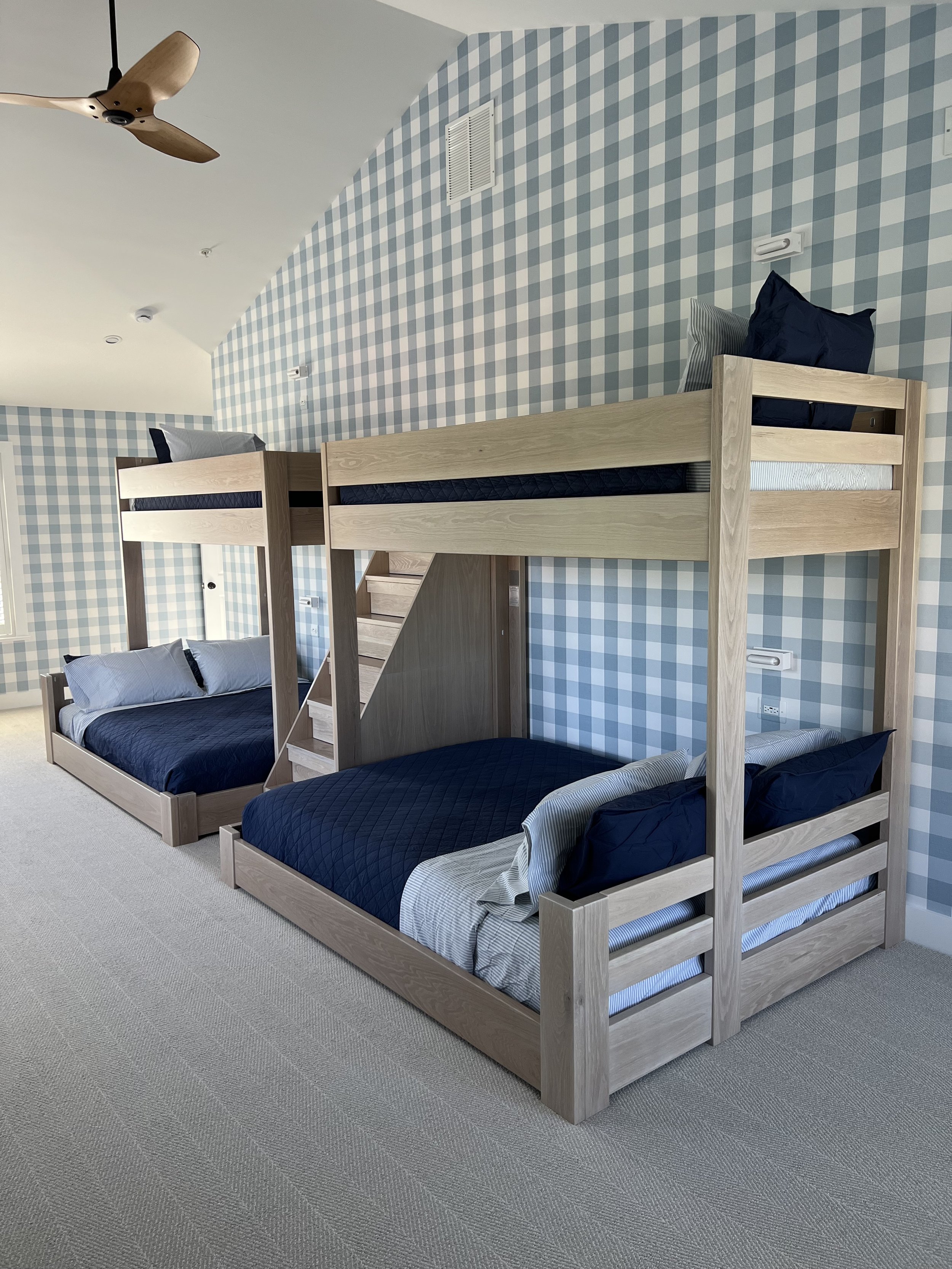 Bedroom with two bunk beds, one on the floor and one elevated, against a blue and white checkered wall, with a ceiling fan.