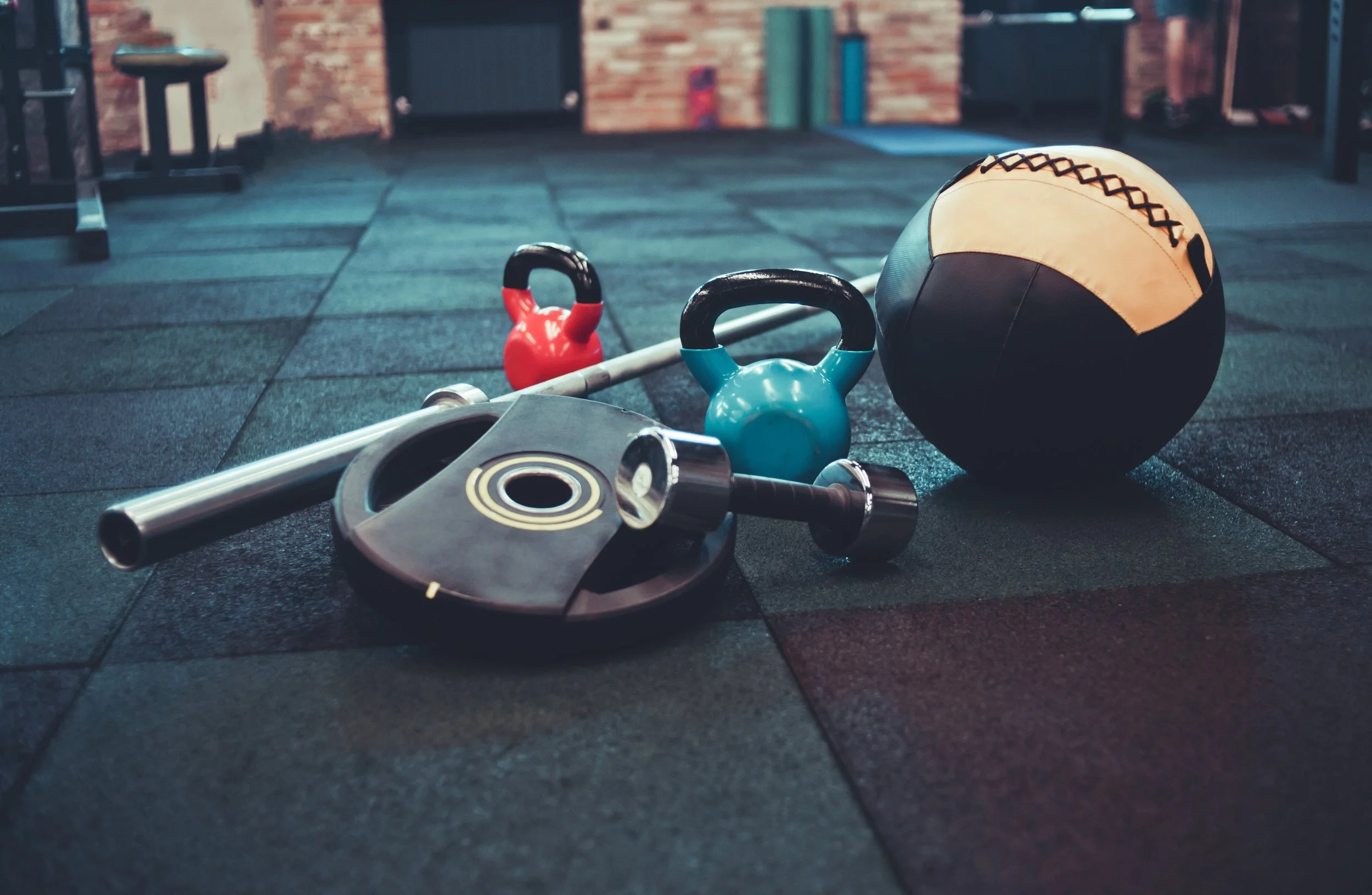 Workout equipment on the gym floor, including a kettlebell, a medicine ball, and a weight plate.