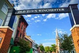 Archway with sign reading 'Old Town Winchester' over a street with historic buildings and a church steeple in the background.
