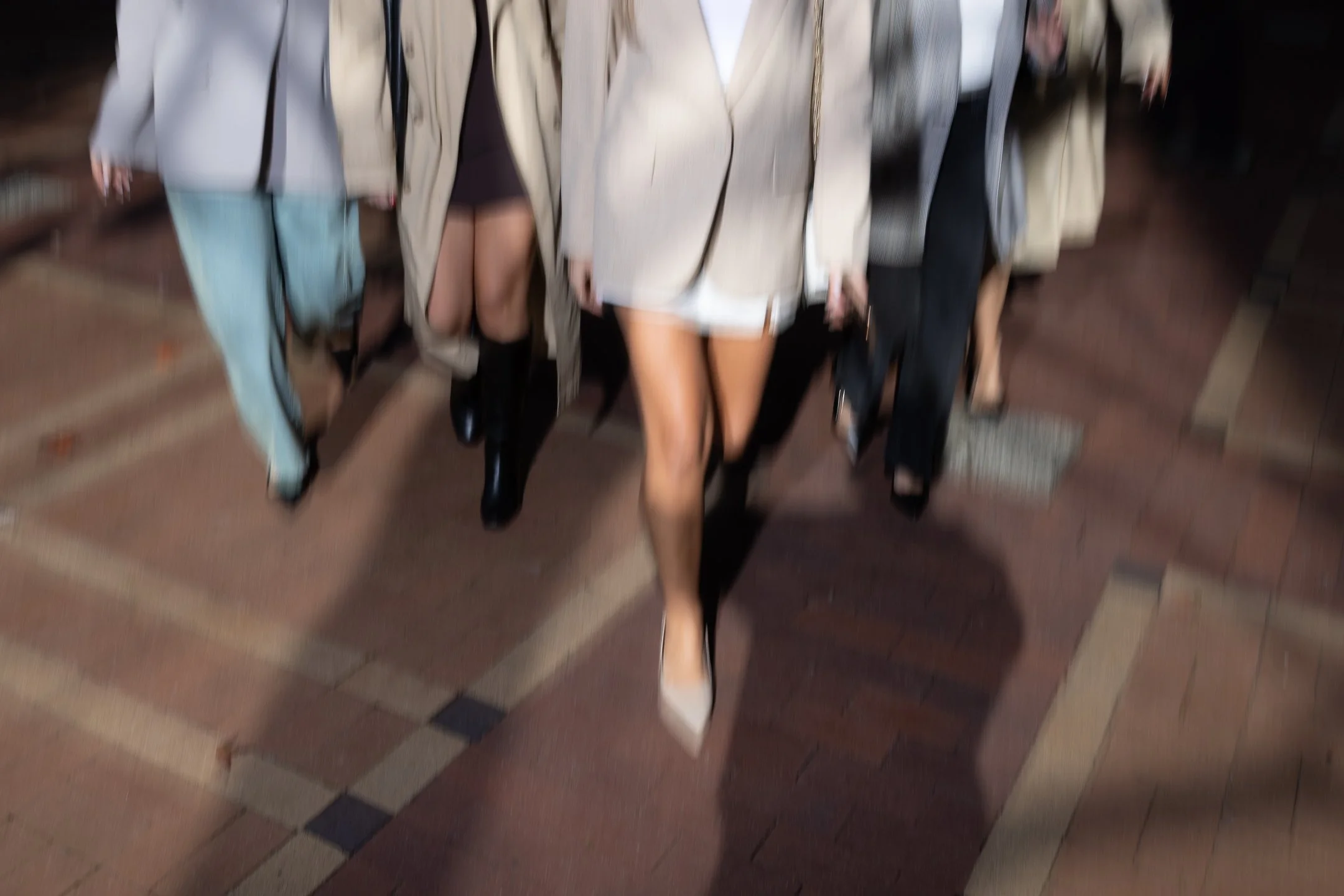 Group of women walking together, viewed from below, showing their legs and shoes, with some dressed in heels and boots.