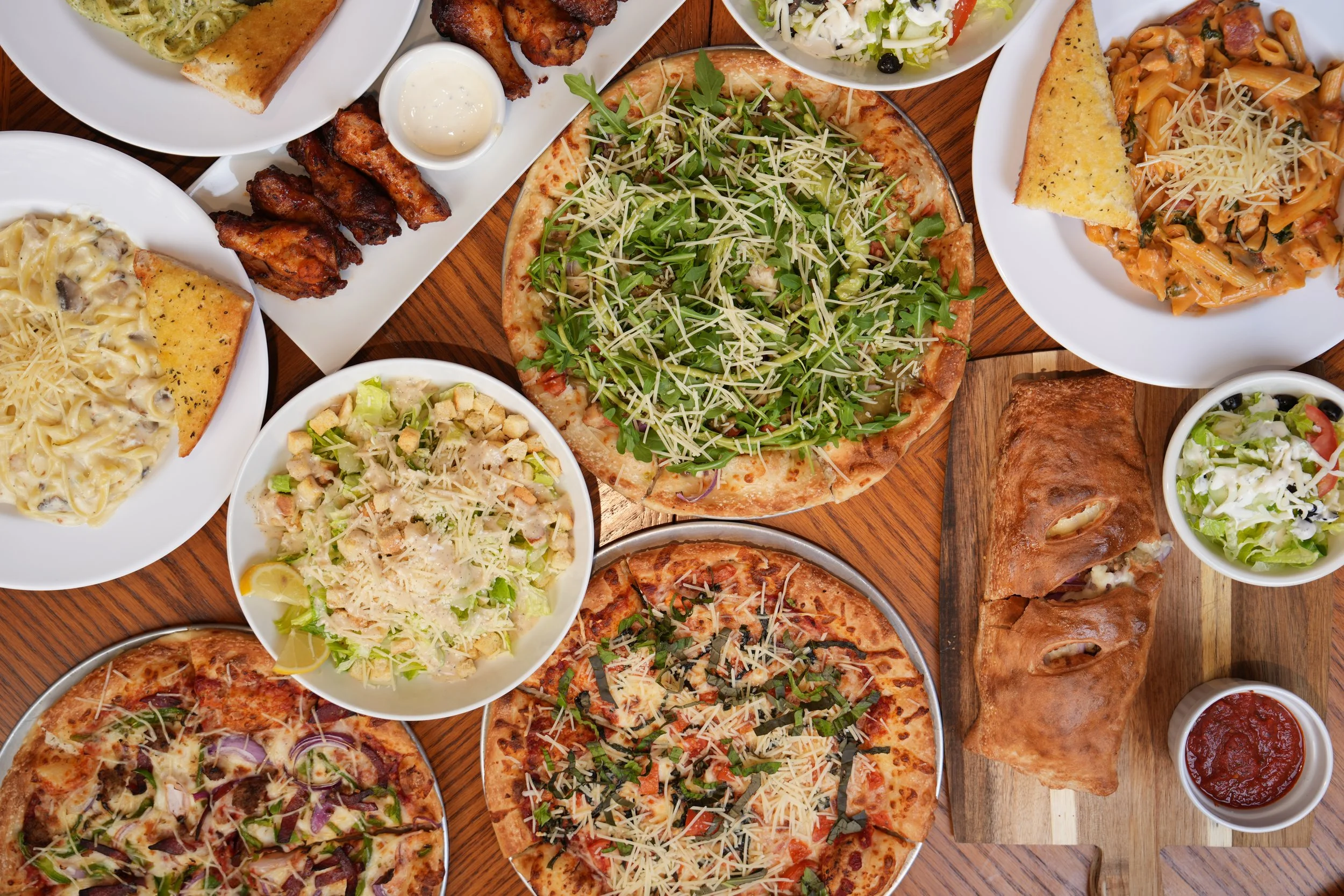 An overhead spread of fresh pizzas, pasta and salads at Castello Pizza & Pasta, a gluten-free-friendly pizza kitchen on Rainier Ave S in South Seattle