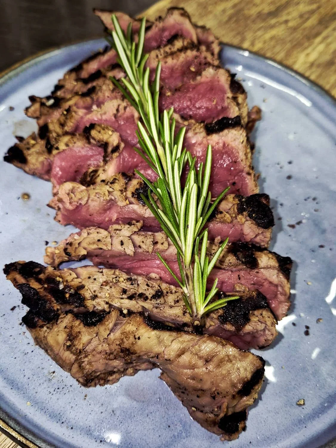 Faux filet de bœuf saignant avec une branche de romarin sur une assiette bleue - Aftersport Clavier