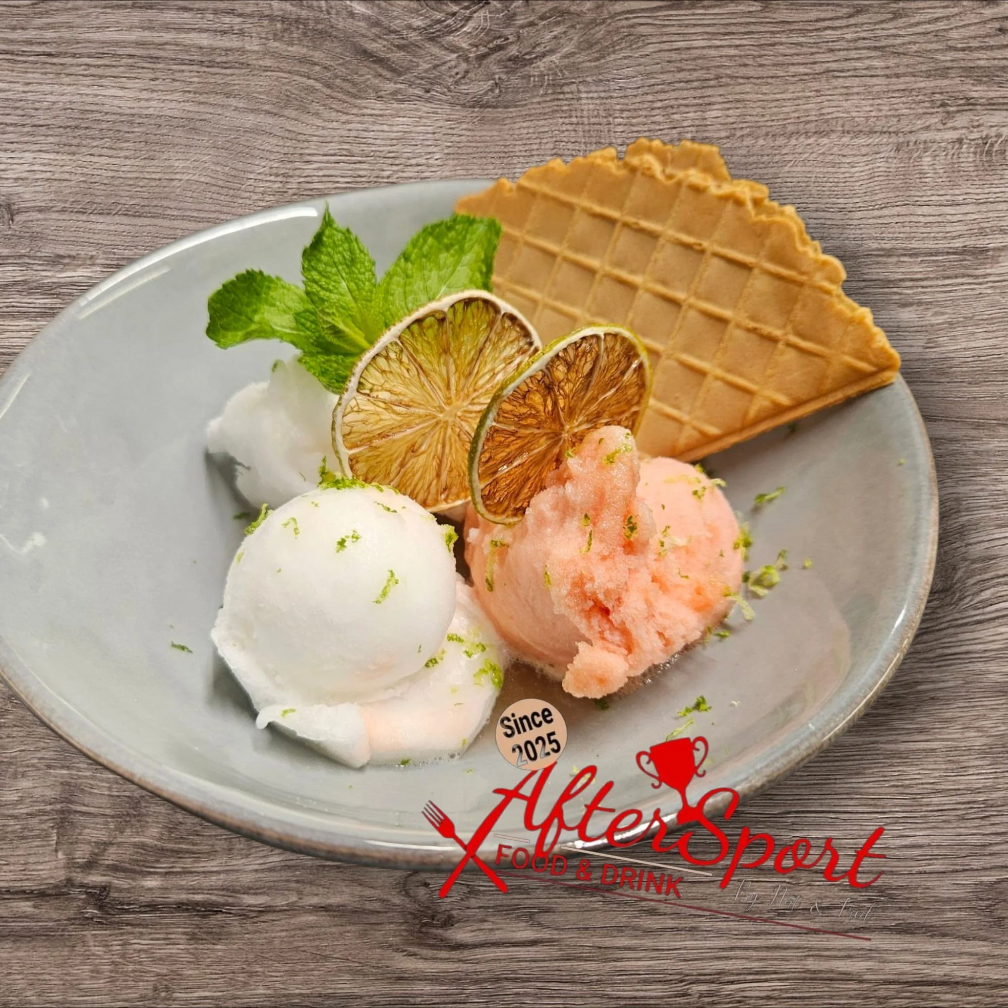 Dessert avec deux boules de glace, une à la vanille et l'autre à la pêche, accompagnée de tranches de citron séchées, de feuilles de menthe, d'une gaufrette, et d'une garniture de crème - Aftersport Clavier