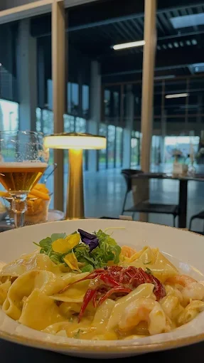 Plat de pâtes avec sauce, légumes, et garnitures, dans un restaurant moderne avec vue sur l'extérieur  - Aftersport Clavier