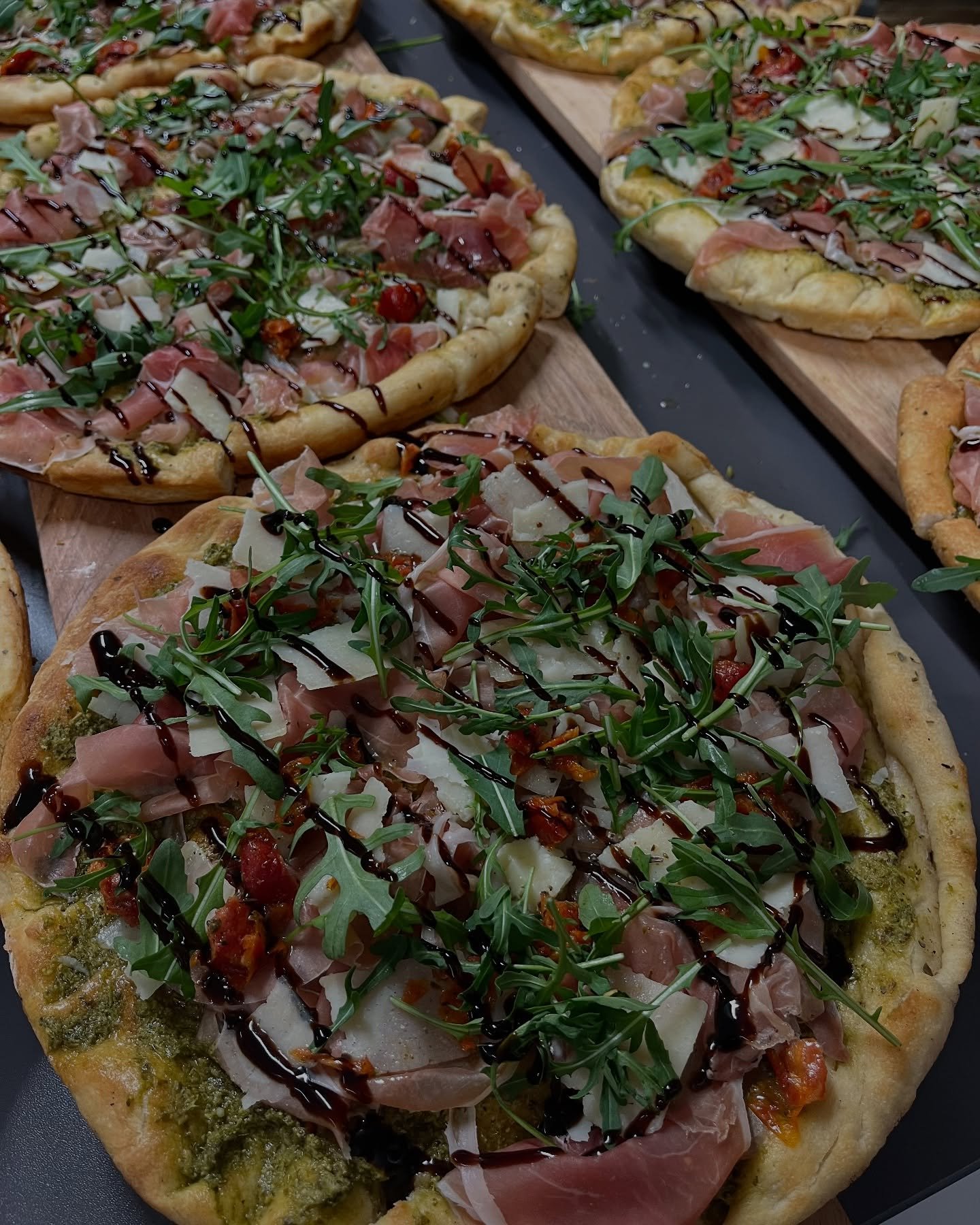 Pizza garnie de jambon, roquette, parmesan, tomate, et sauce balsamique, sur une surface en pierre  - Aftersport Clavier