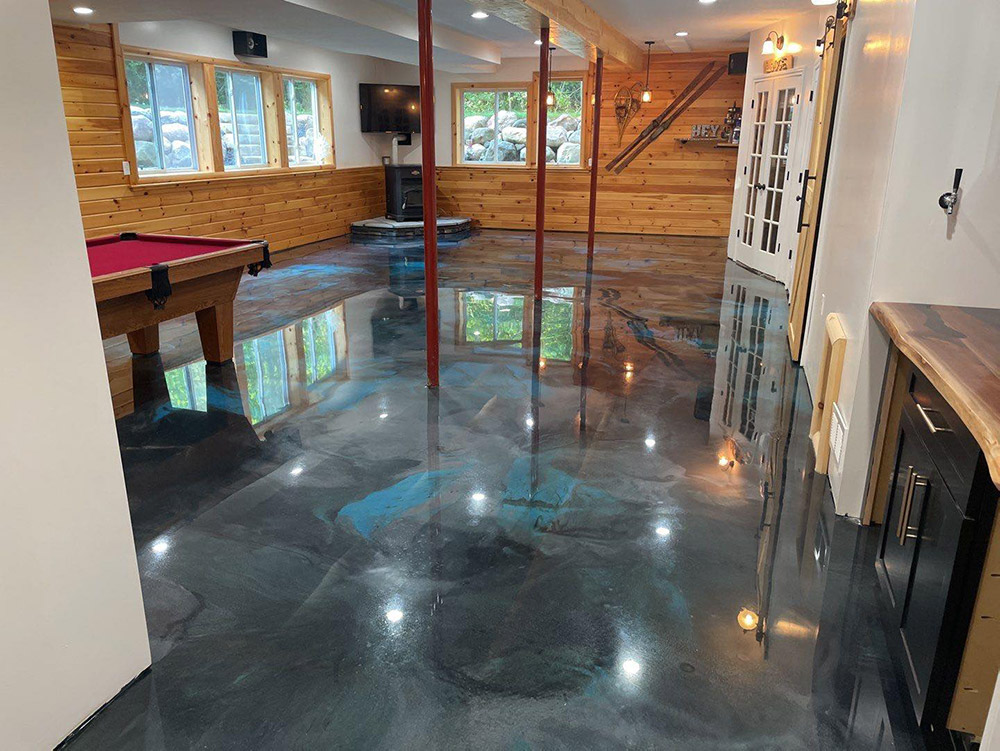 Interior of a finished basement with a polished, reflective concrete floor, wooden walls, multiple windows, a pool table, a TV mounted on the wall, and a corner fireplace.