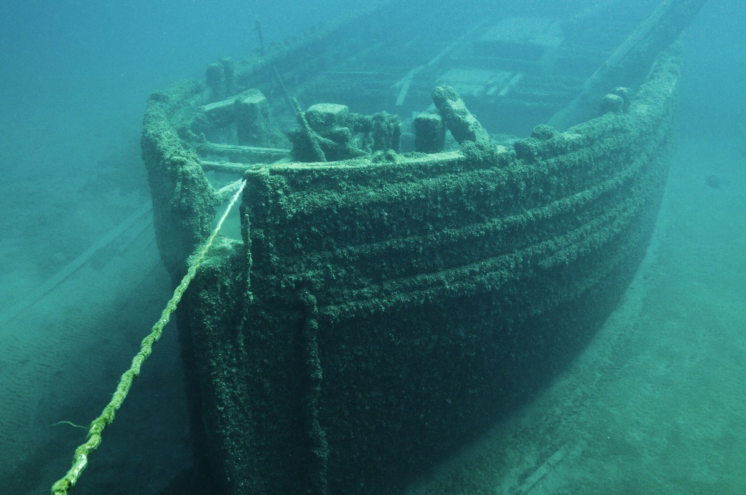 An underwater photo of a sunken shipwreck, covered in algae and marine growth, resting on the seafloor with untold treasures waiting in its bowels.