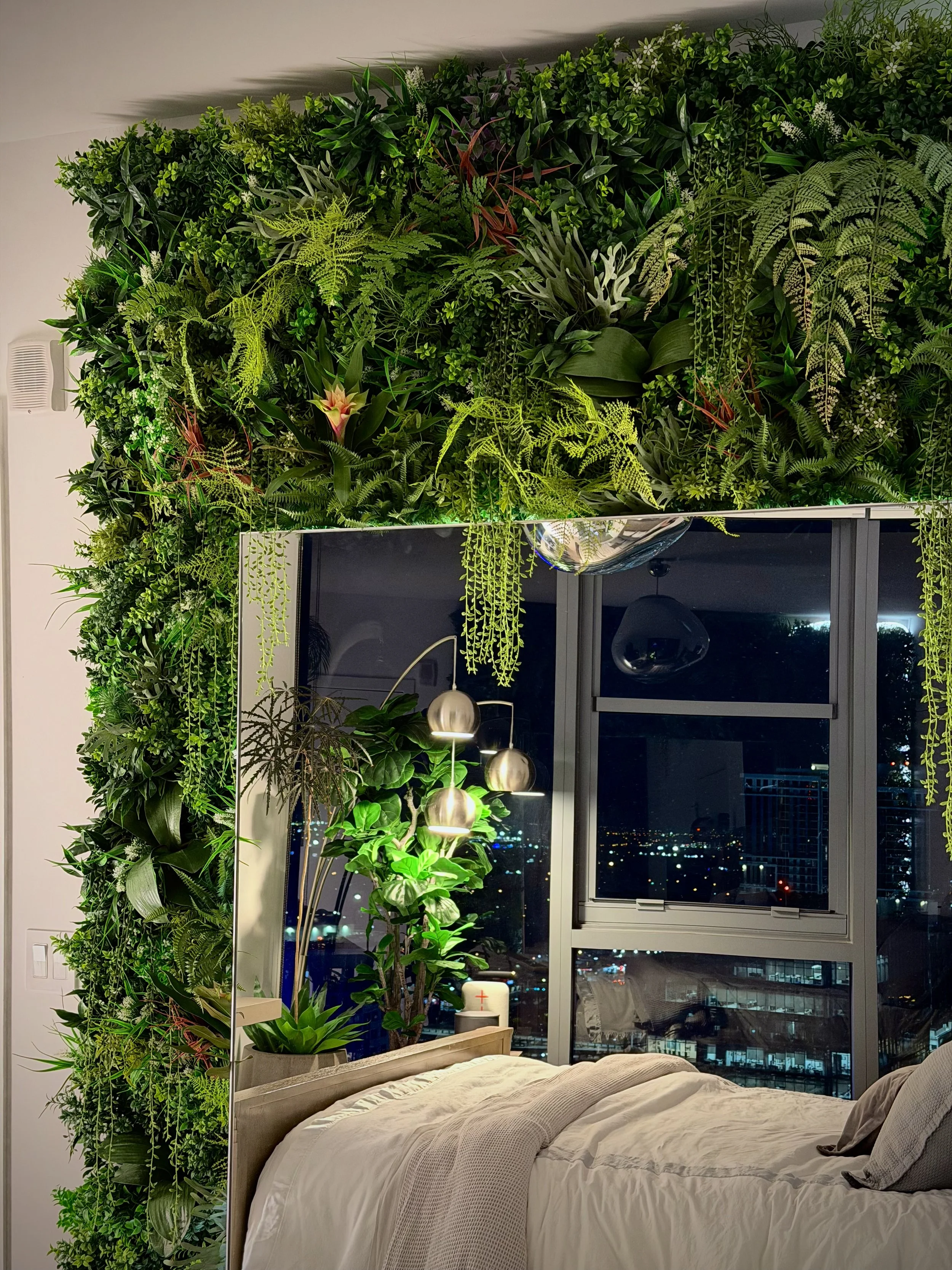 A large standing floor mirror leaning against a lush tropical custom-made plant wall.