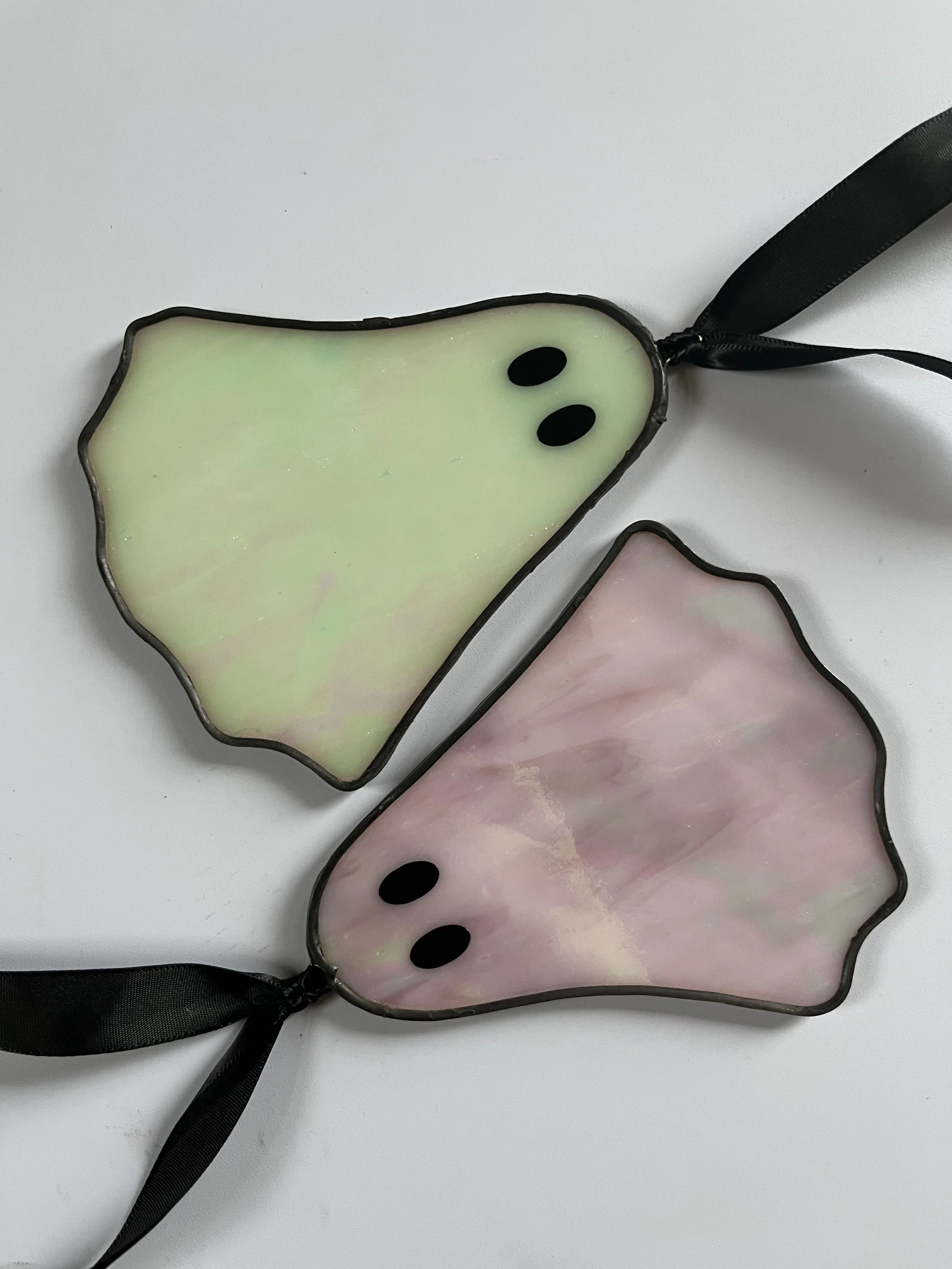 Two pastel-coloured, iridescent ghosts with black ribbon ties on a white surface.