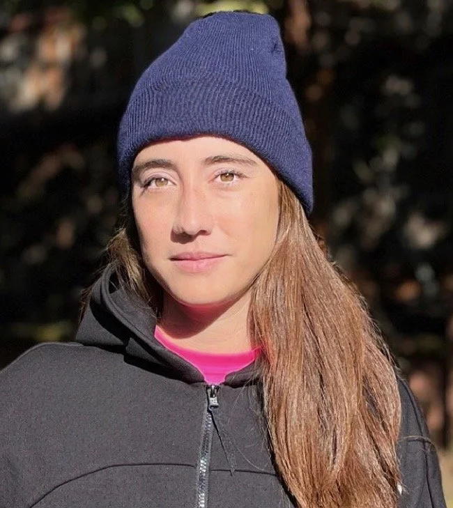 Young woman wearing a navy knit beanie and black jacket outdoors