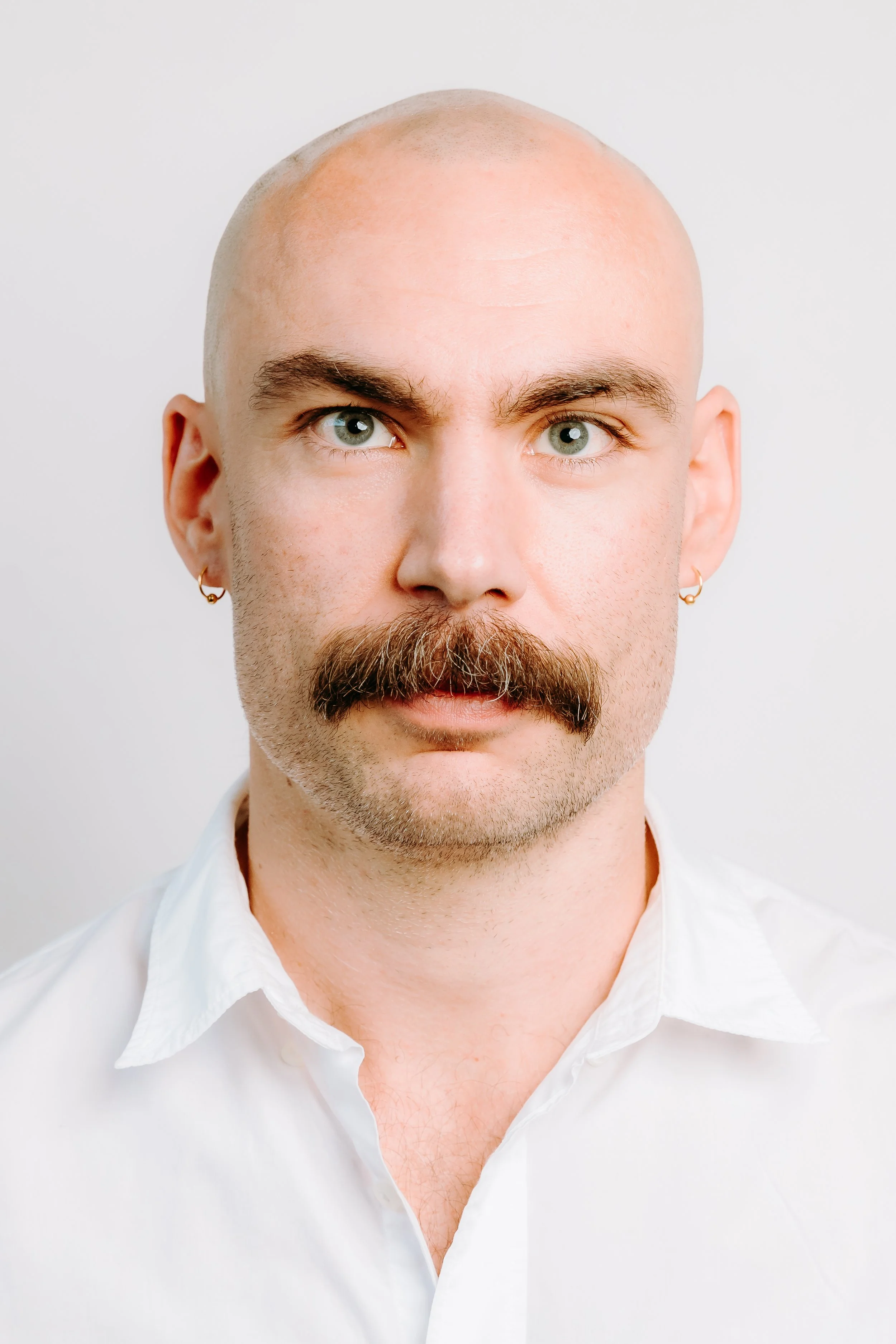 An image of Tom Richards. here is wearing a white shirt, he is looking off camera, he has a moustache.